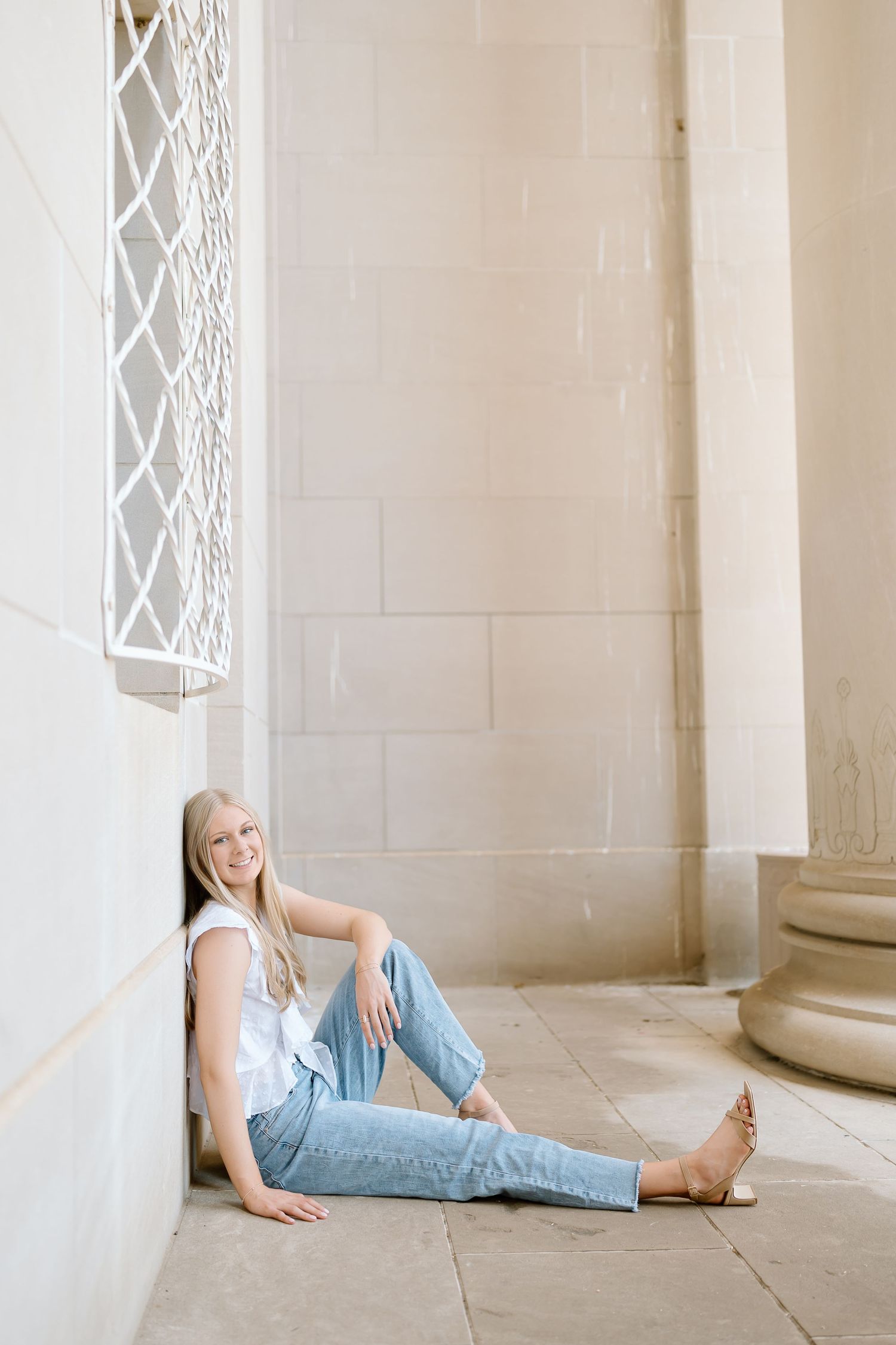 Person in light blue jeans lying on a marble floor against white stone columns in an elegant architectural setting.