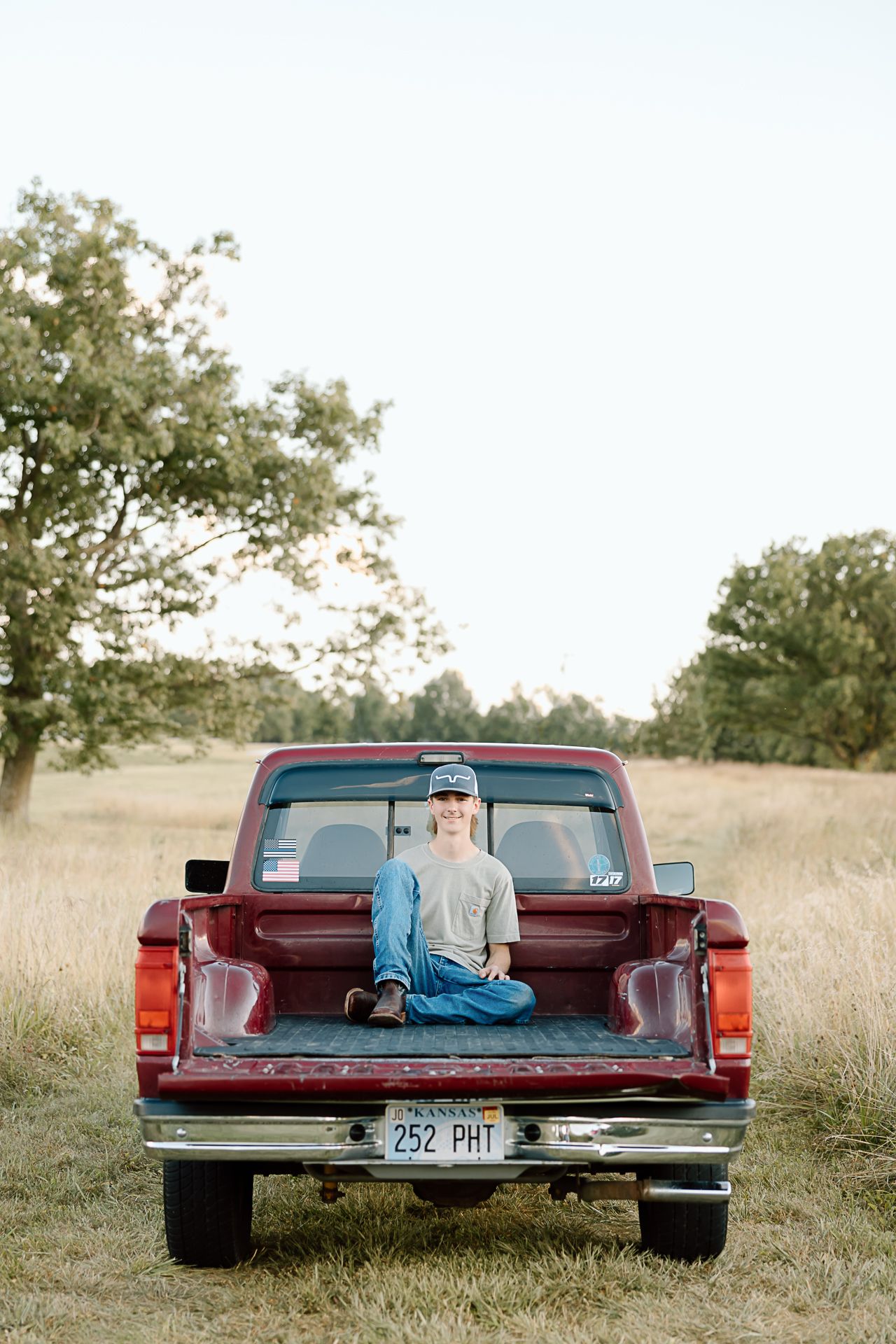 A vintage red pickup truck parked in a grassy field at sunset with someone resting in the truck bed.