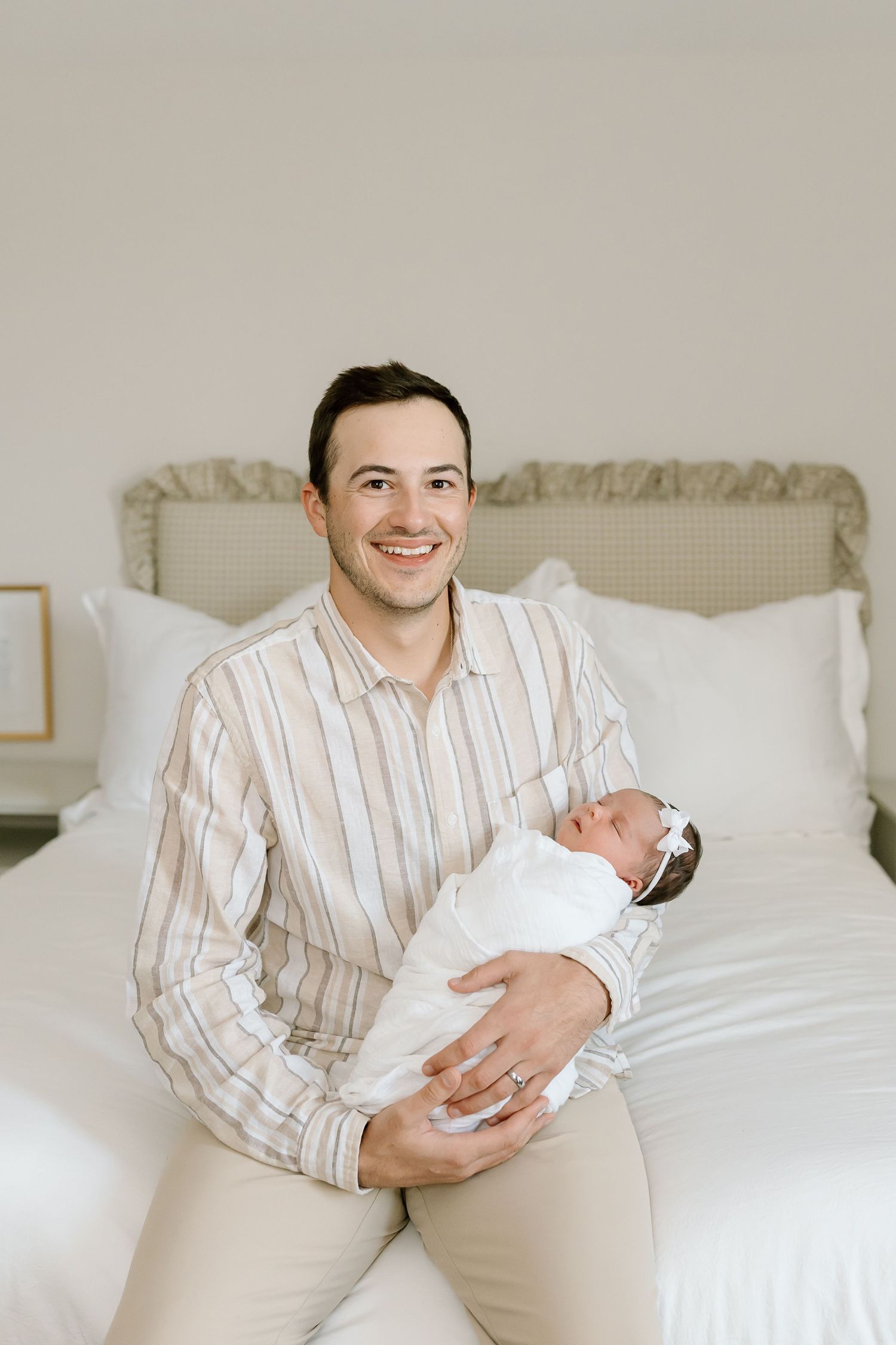 A series of four photos showing someone in a striped shirt holding a baby while sitting on a white bed.