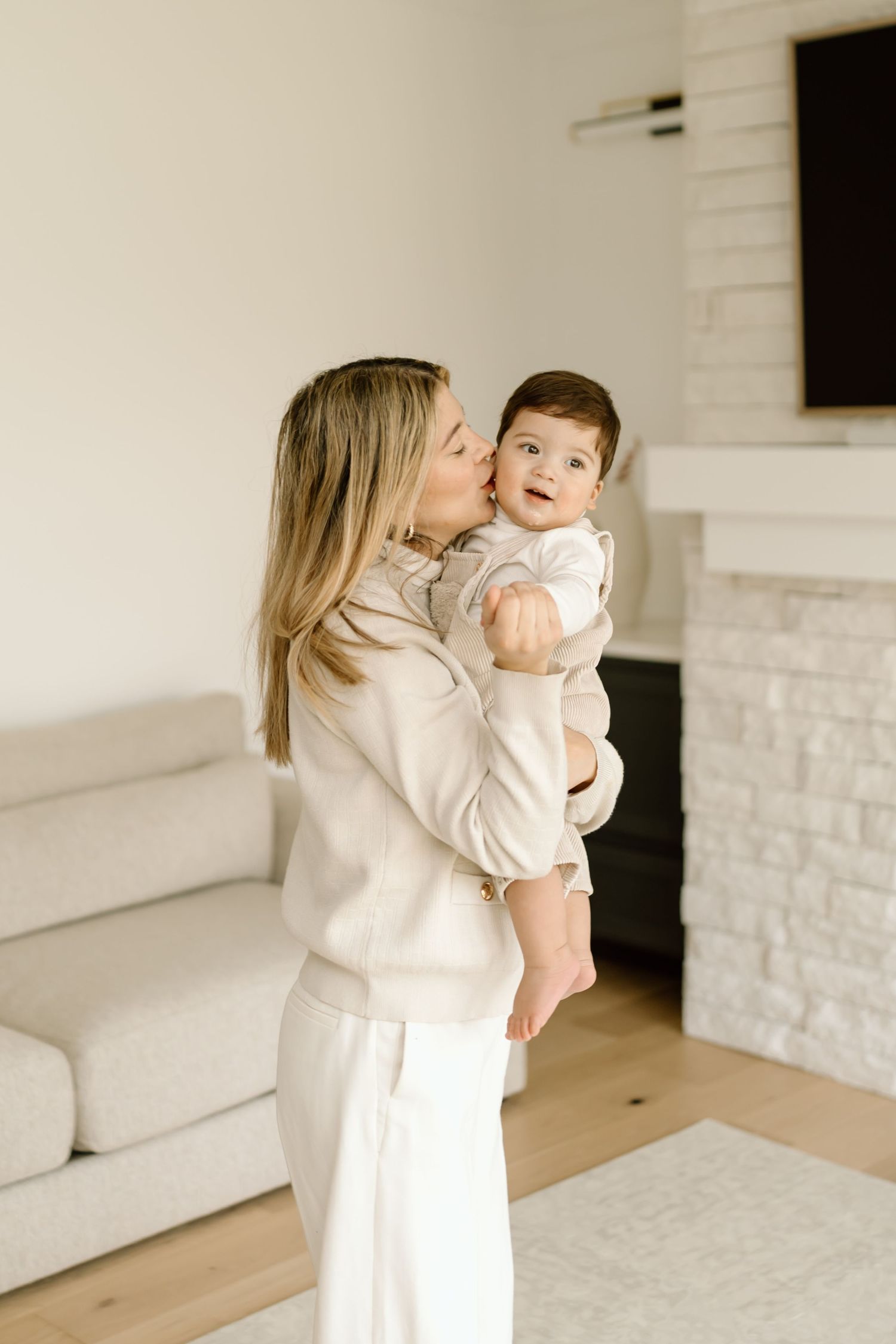 A parent and child wearing white share tender moments together in a bright minimalist room with white brick walls.