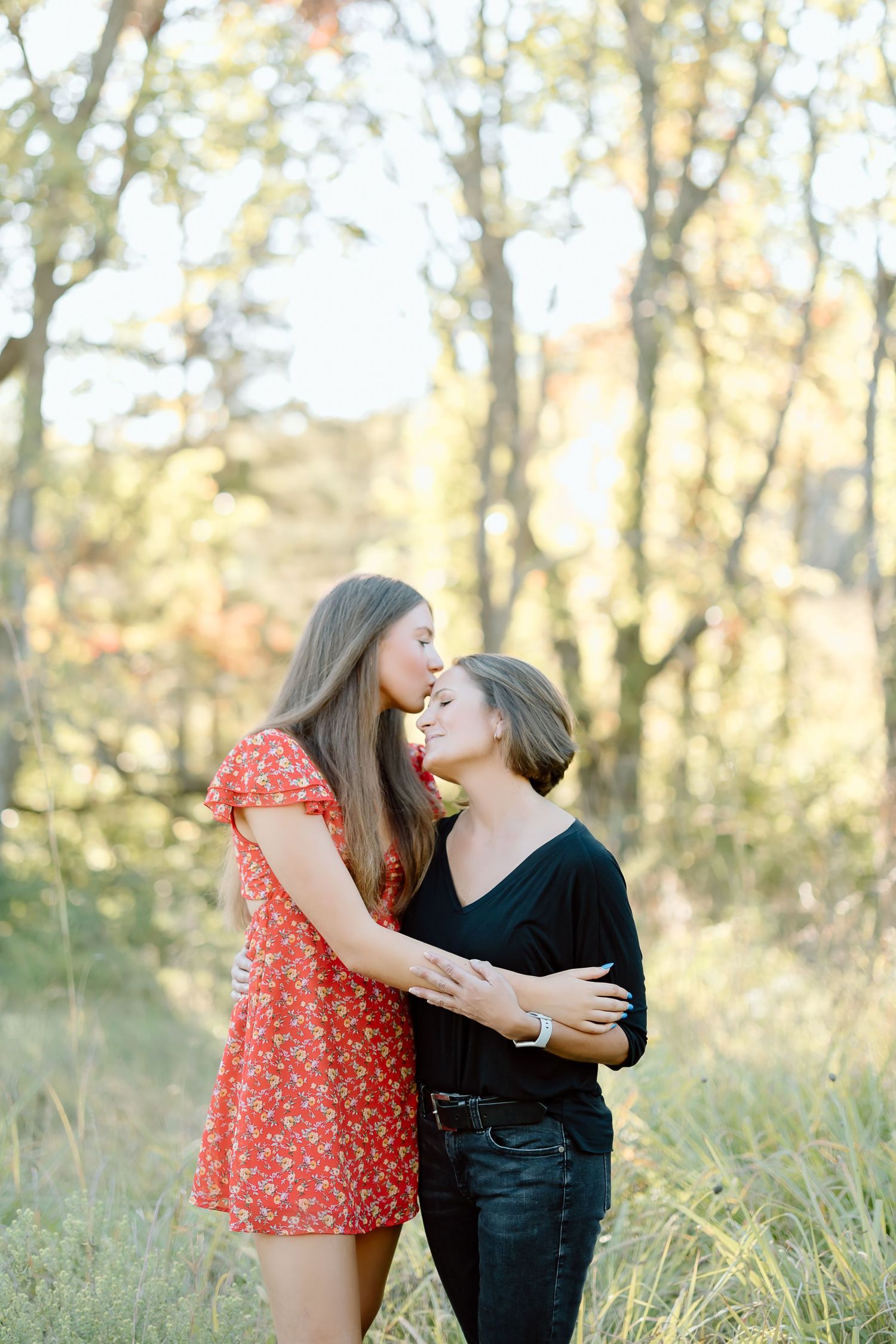 A couple embraces in a romantic moment outdoors among autumn trees and tall grass at sunset.