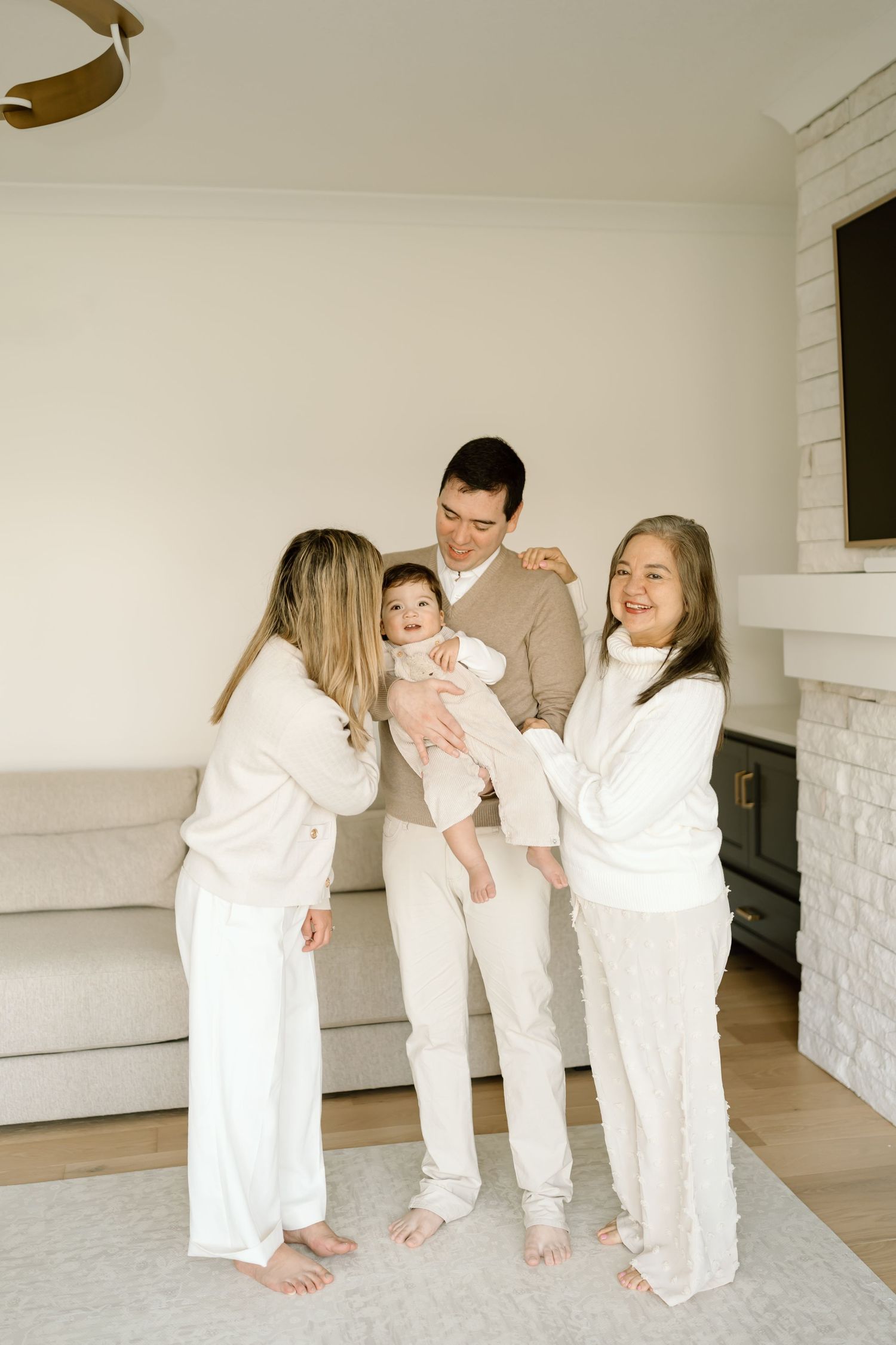 A family wearing matching white outfits stands together barefoot on a light carpet in a modern living room.