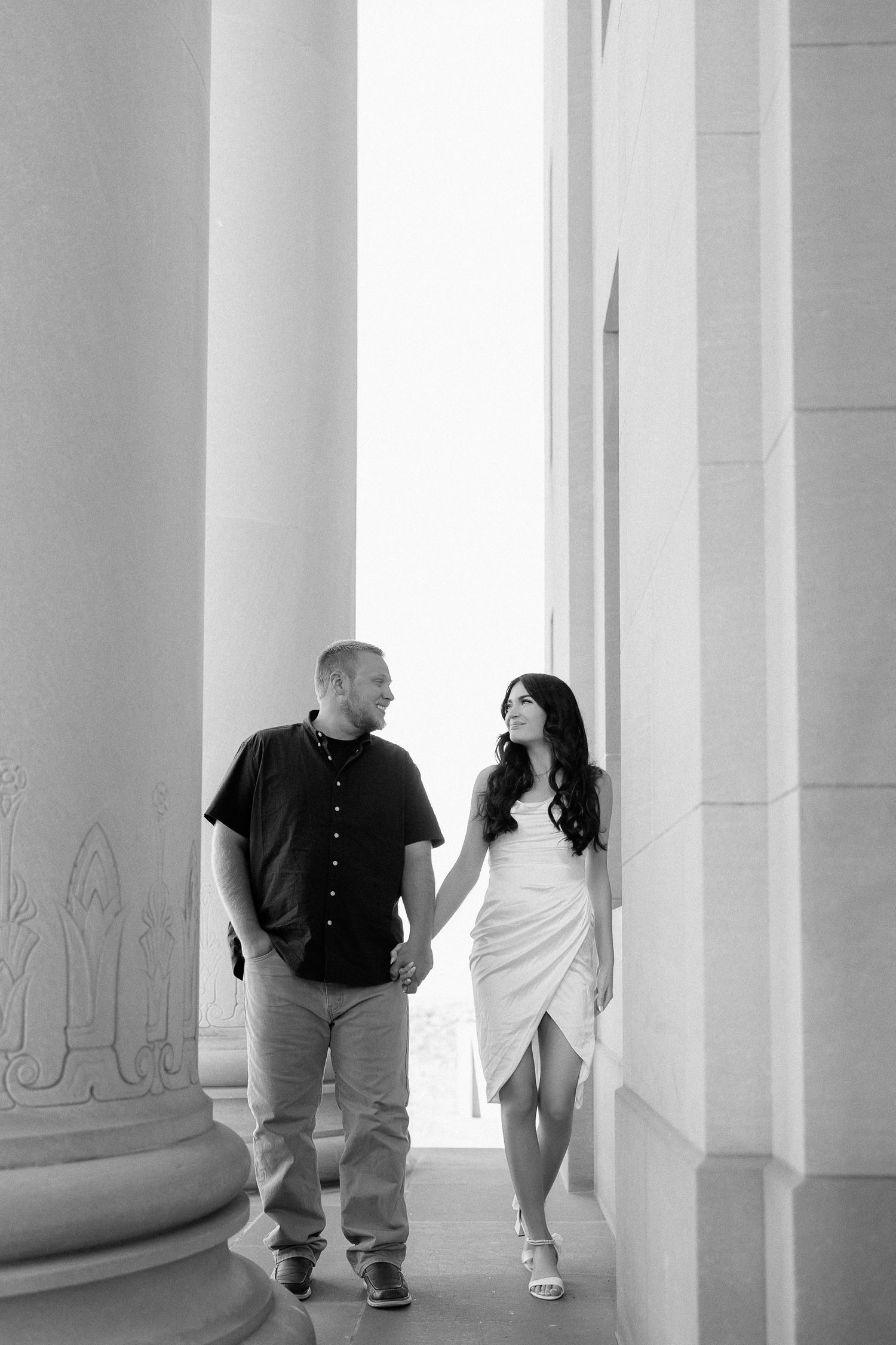 People walk and converse between white architectural columns in a bright minimalist interior space.