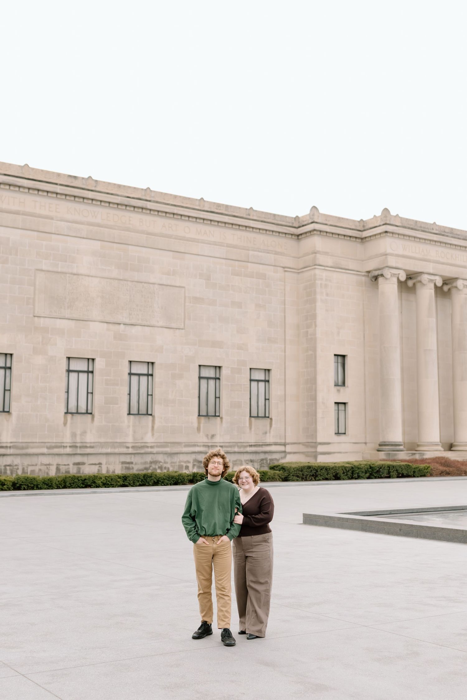 Two people stand outside a grand neoclassical building with limestone walls and columns.