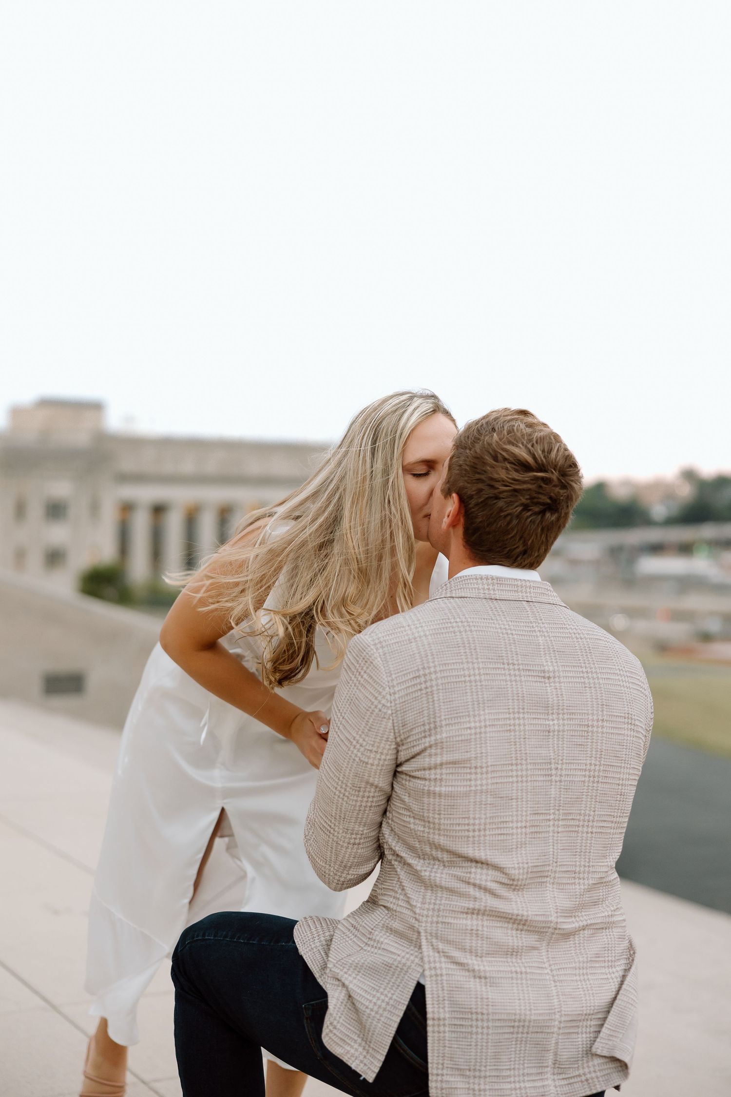 A couple sits together on a stone ledge overlooking a city view in a romantic moment.