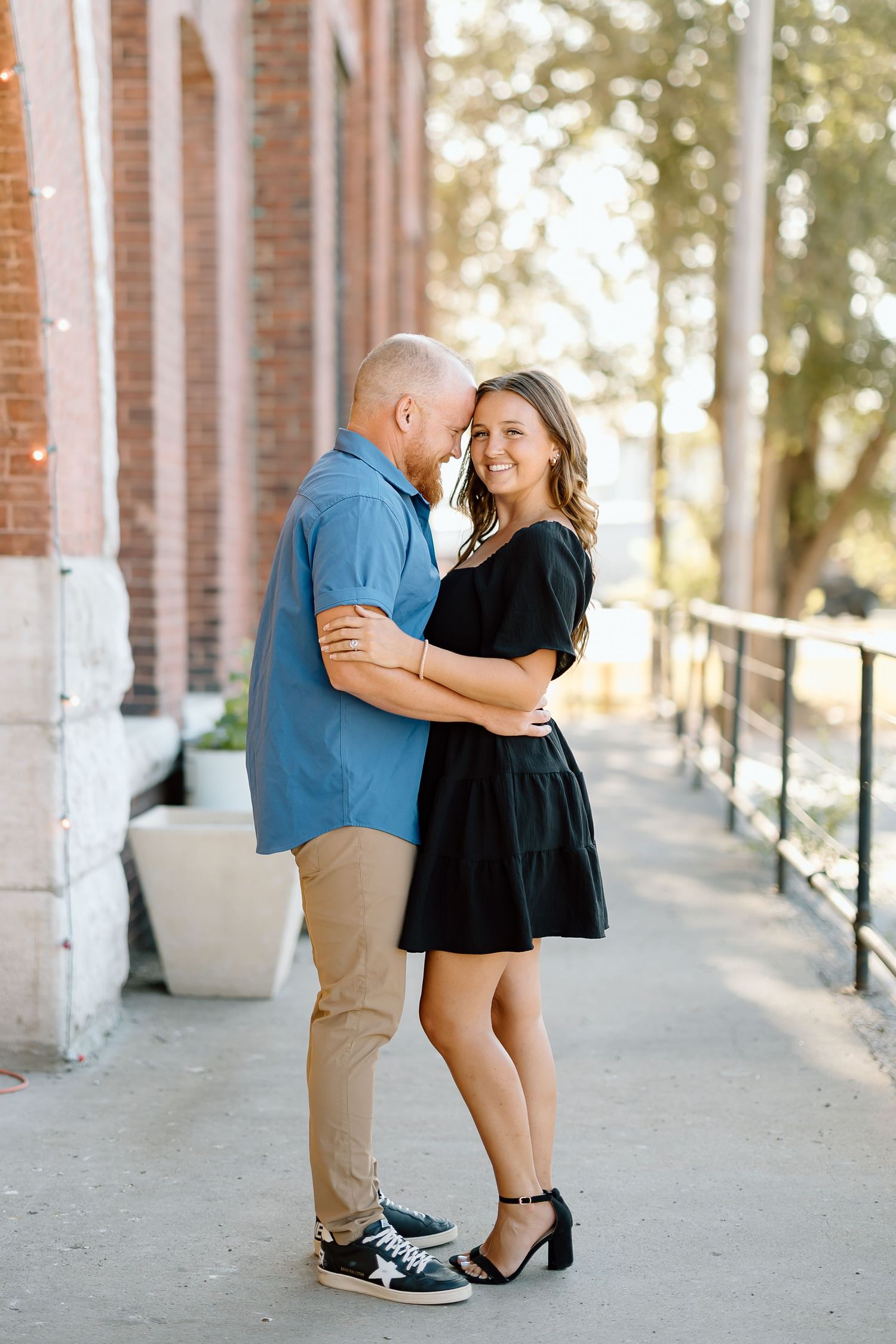 A couple shares romantic moments under white columns in a covered walkway during a sunny afternoon photoshoot.