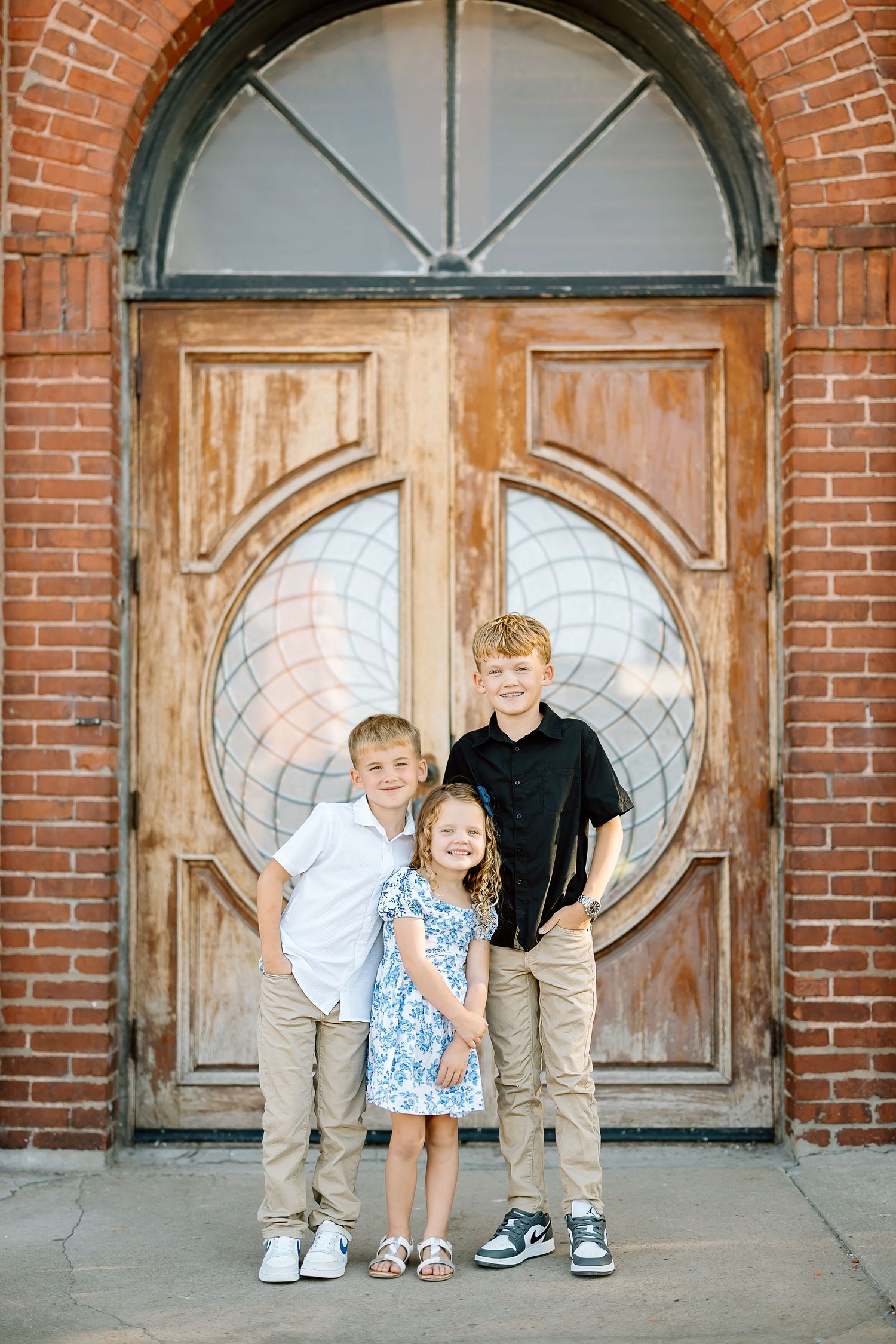 Three candid photos showing children sitting and standing in front of rustic wooden doors with brick archways.