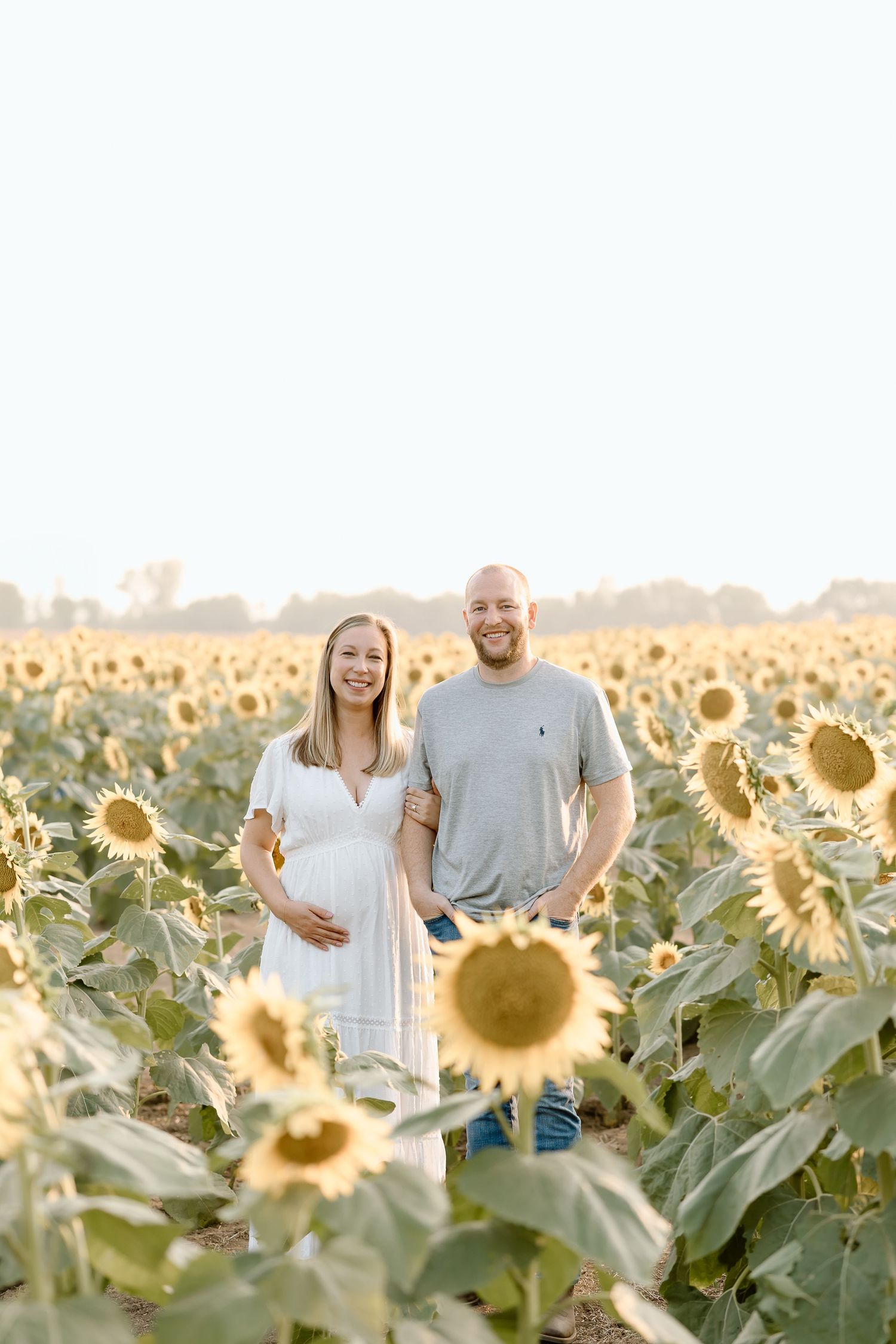 A couple poses together in a vibrant sunflower field during golden hour creating a romantic summer scene.
