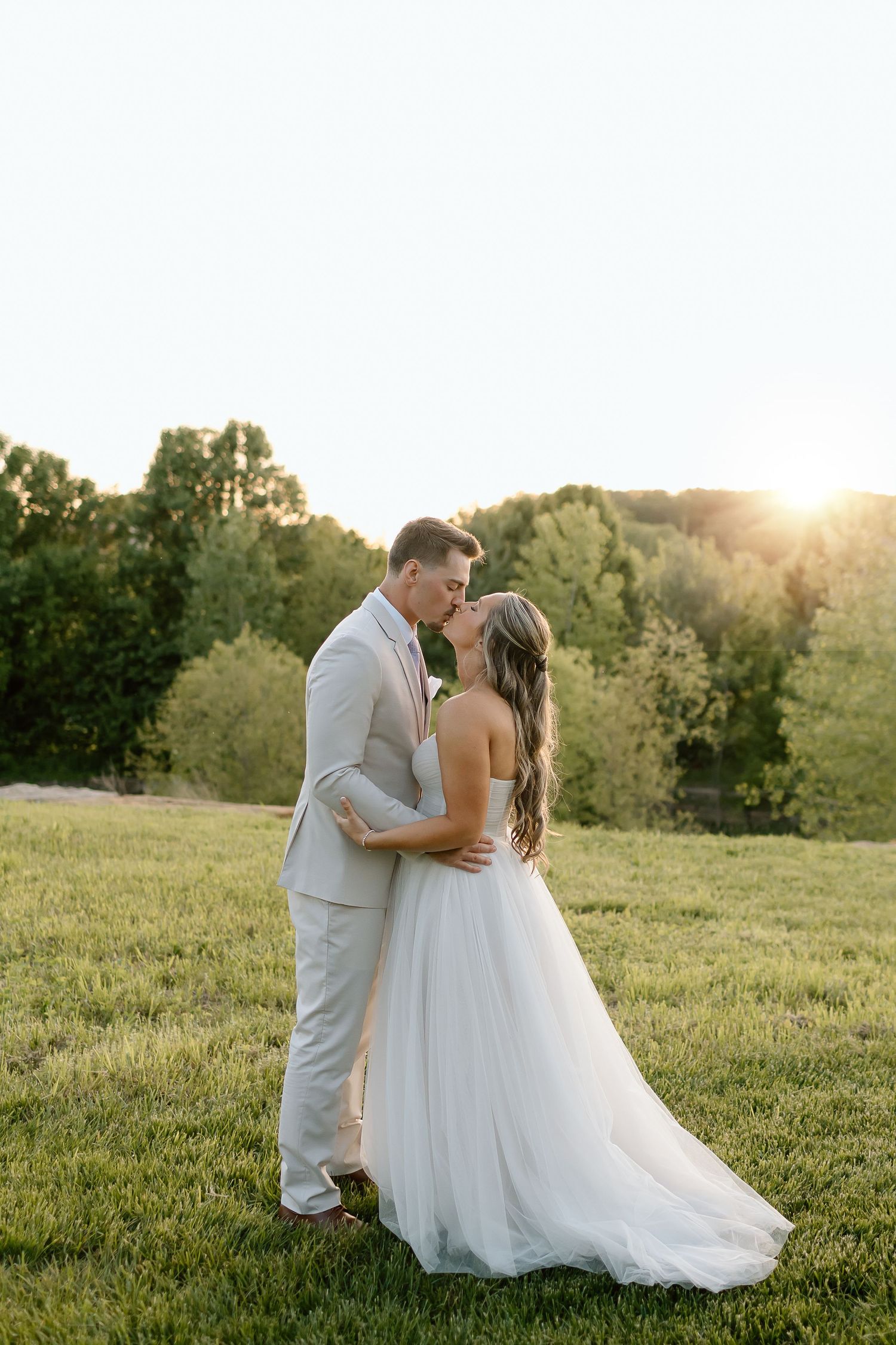 Newlyweds share an intimate moment during sunset photos in a grassy field.