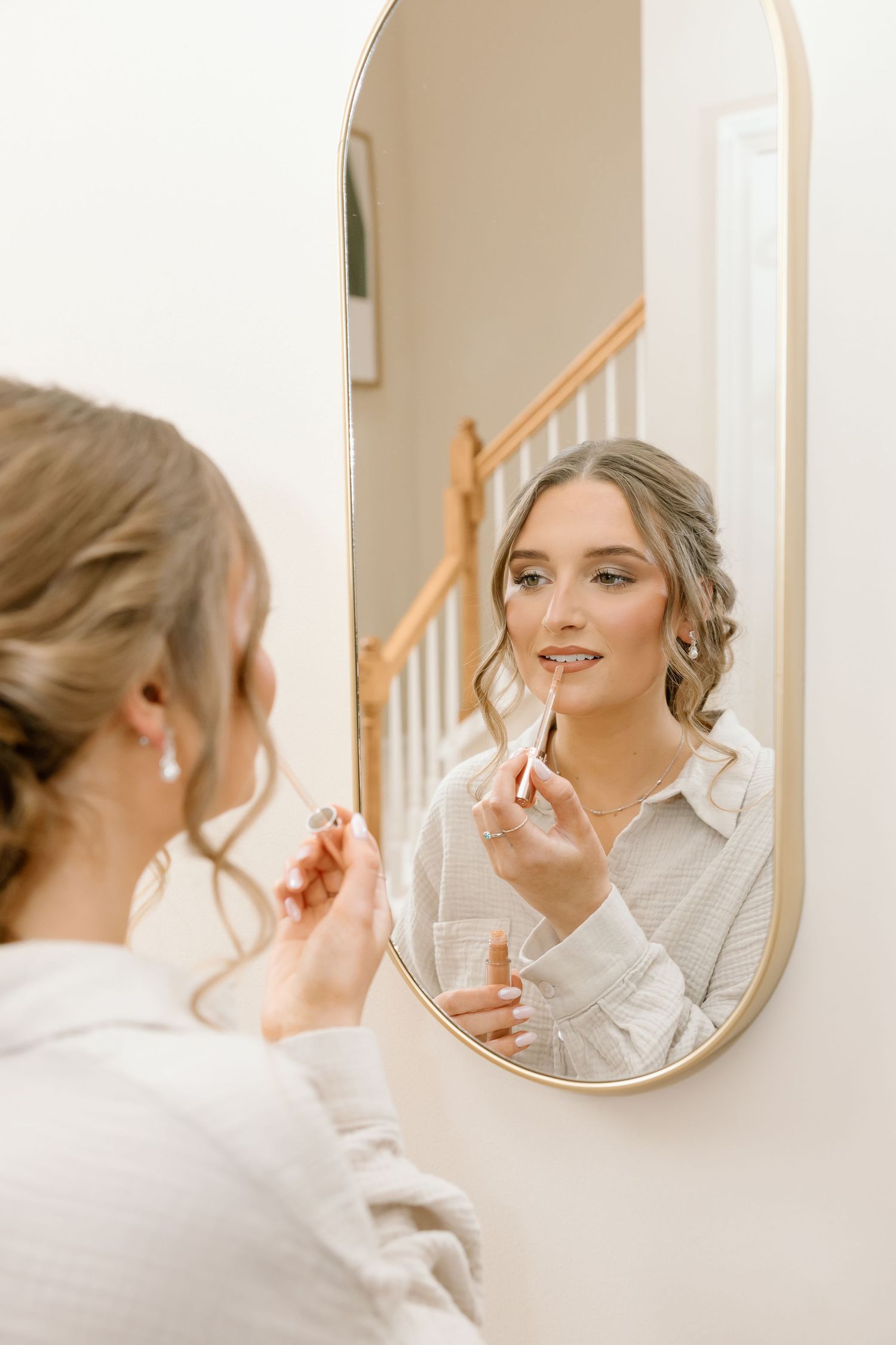 Someone applying makeup while looking in an oval mirror mounted on a white wall.