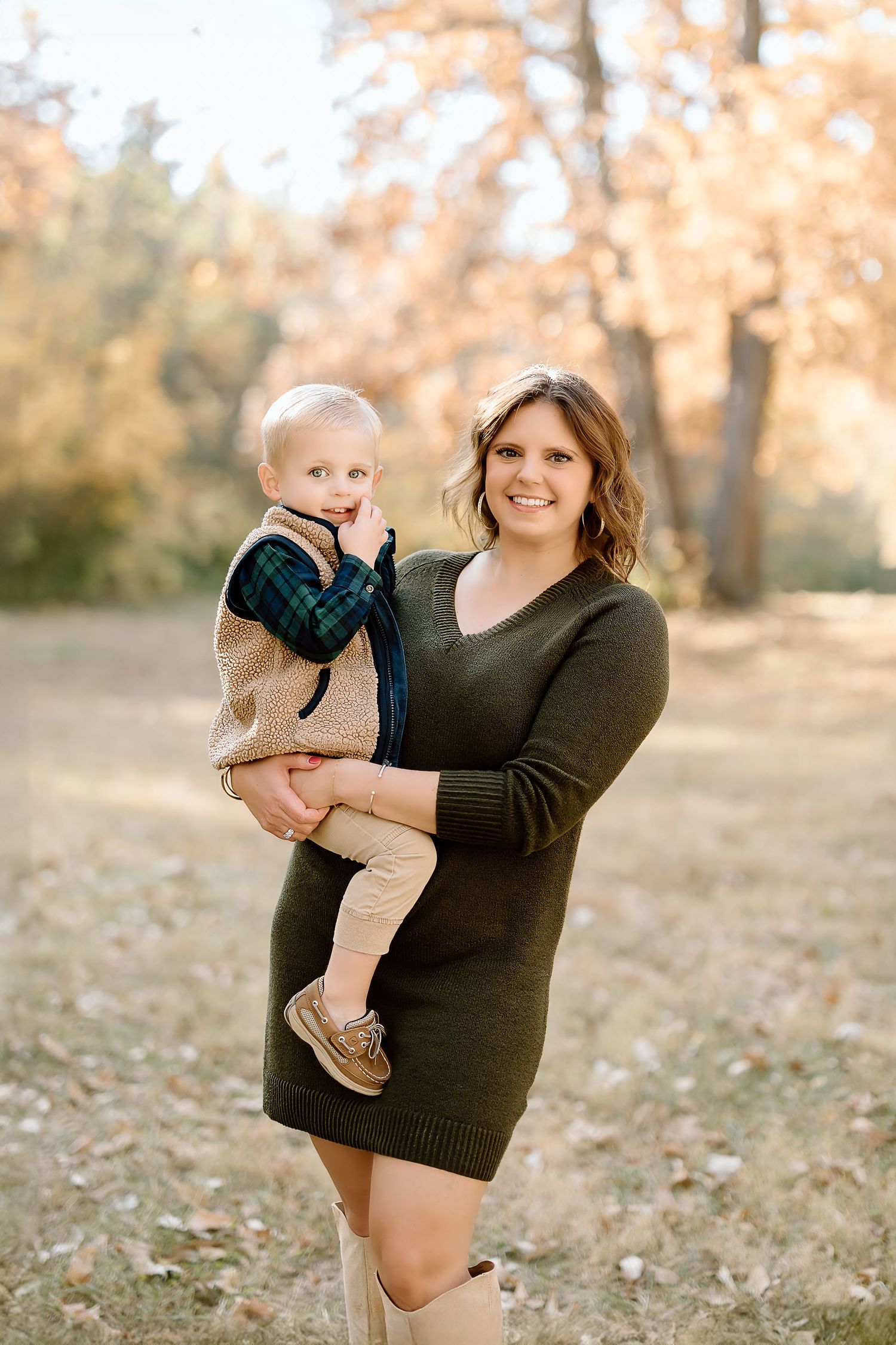 A parent wearing a sweater dress holds a toddler in casual clothing during a fall photoshoot.
