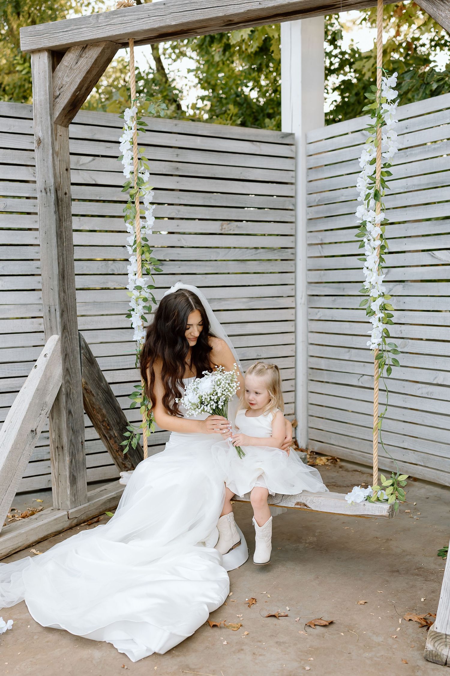 A sequence of three tender moments captured in a white outdoor setting with hanging floral vines and wooden slat walls.