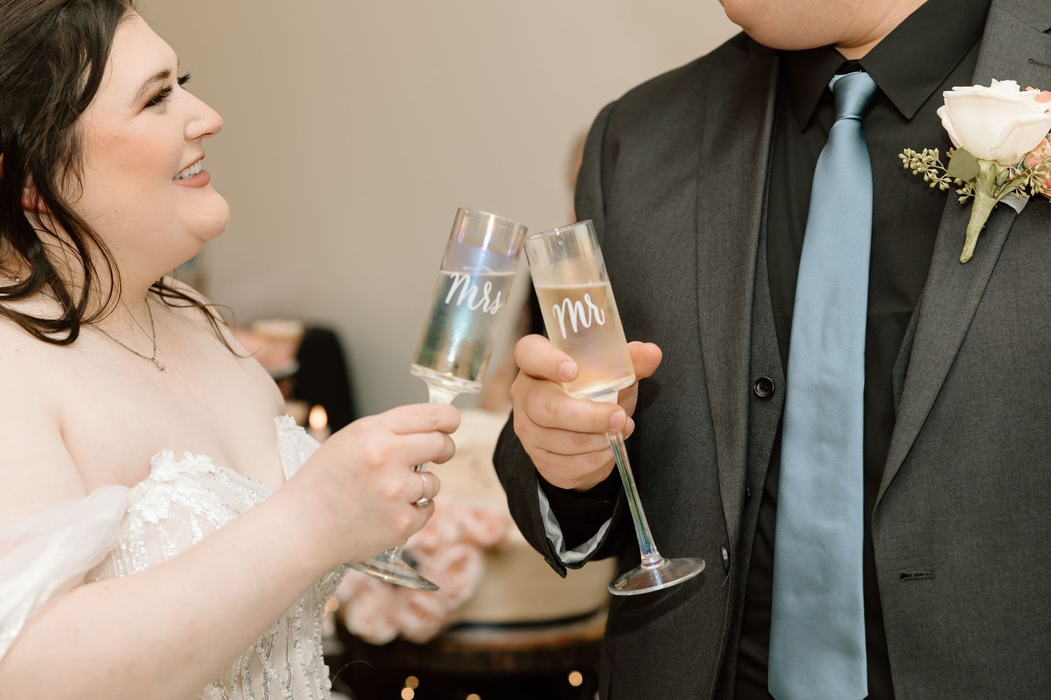Two people toast with champagne flutes at a formal event, with a white rose boutonniere visible on a dark suit.
