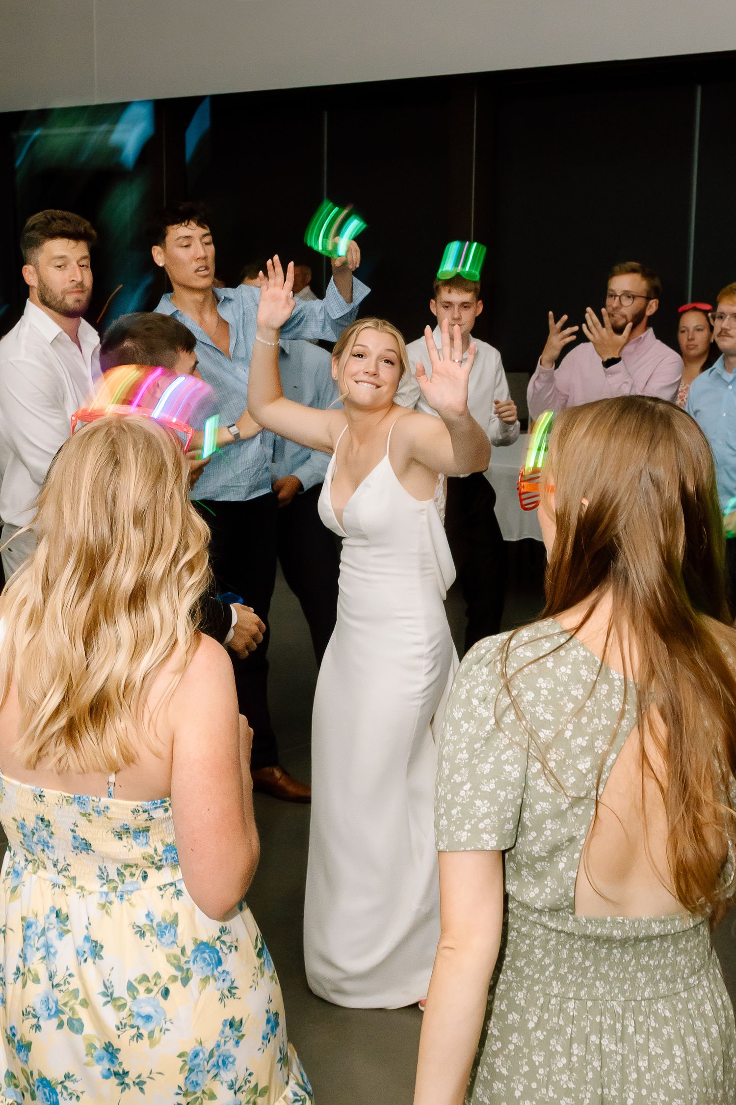 Wedding guests dance and celebrate on a dimly lit dance floor adorned with colorful party lights.
