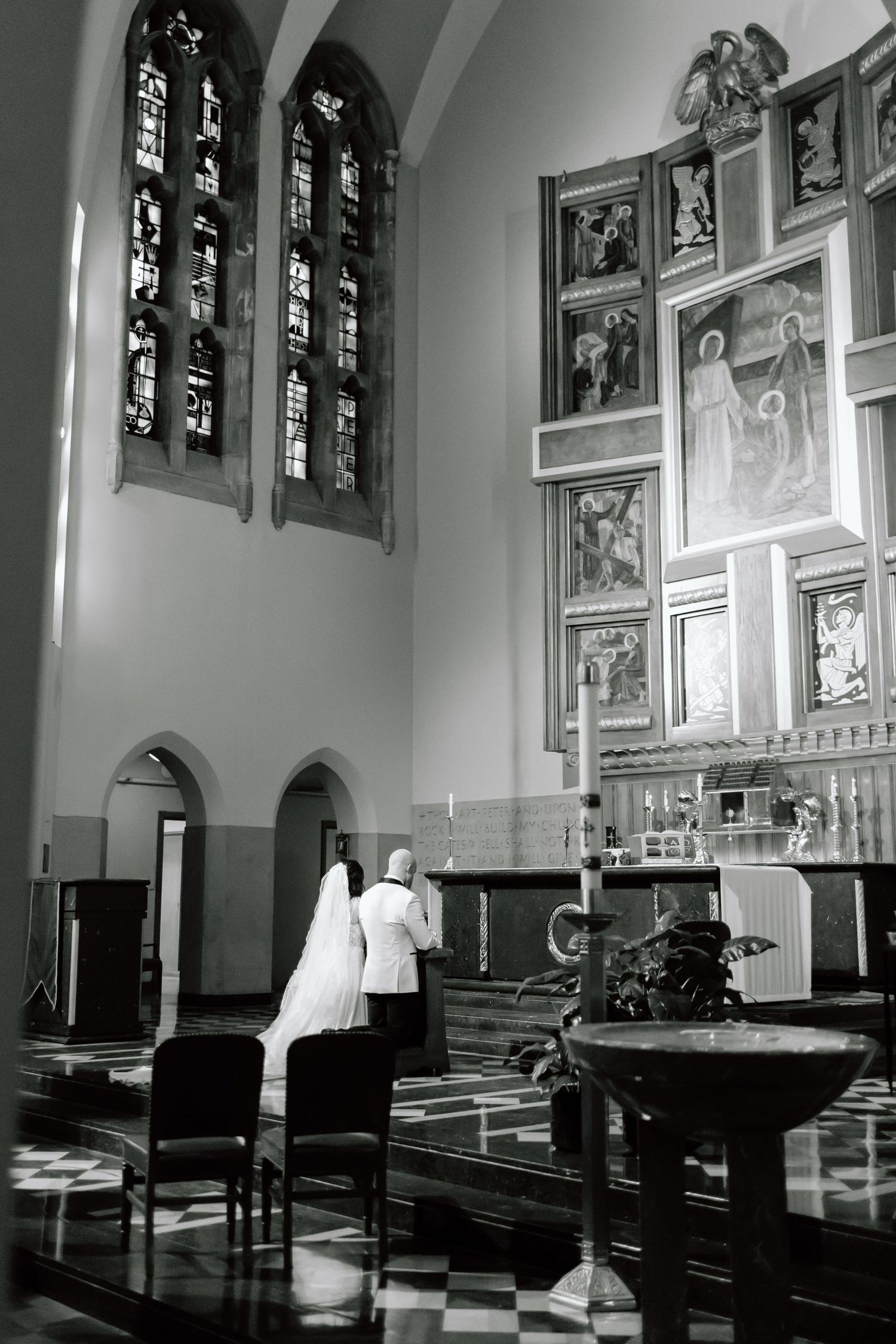 Black and white photo of a church interior with stained glass windows and religious artwork on display.