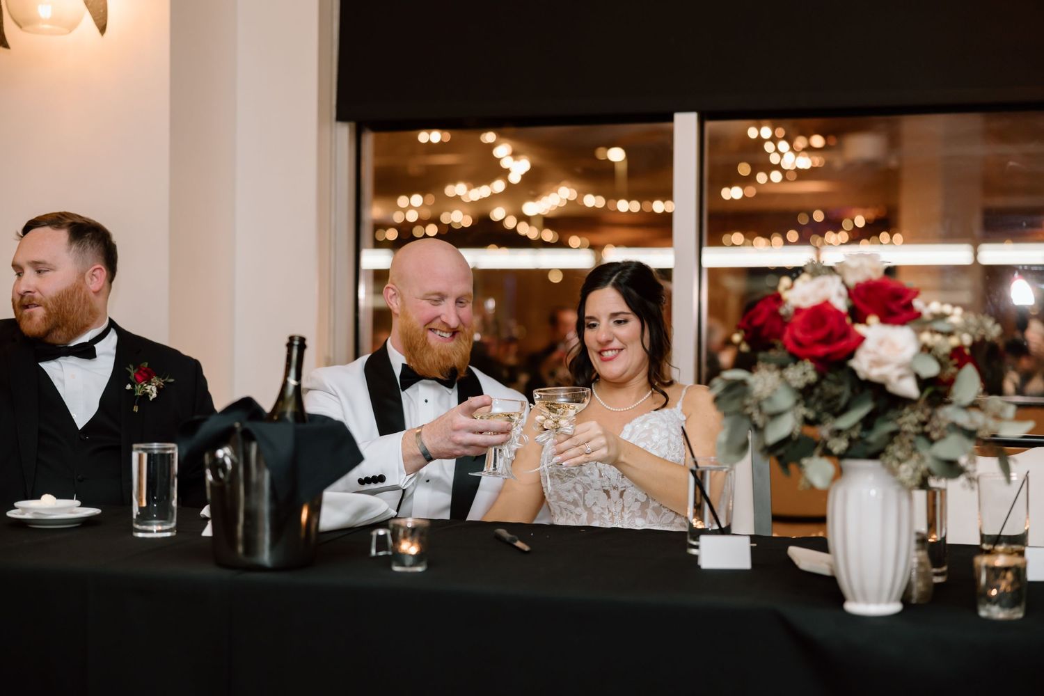 A romantic wedding reception scene with string lights and elegant table settings in a warm indoor venue.