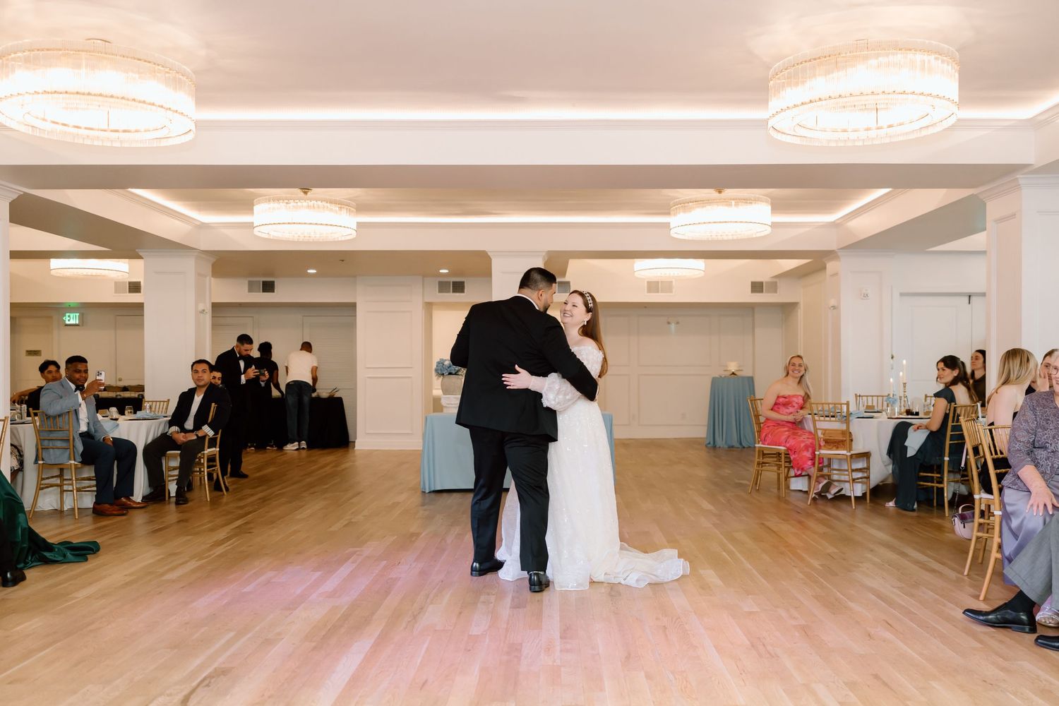 Bride and groom share their first dance on a wooden floor at an elegant wedding reception venue.