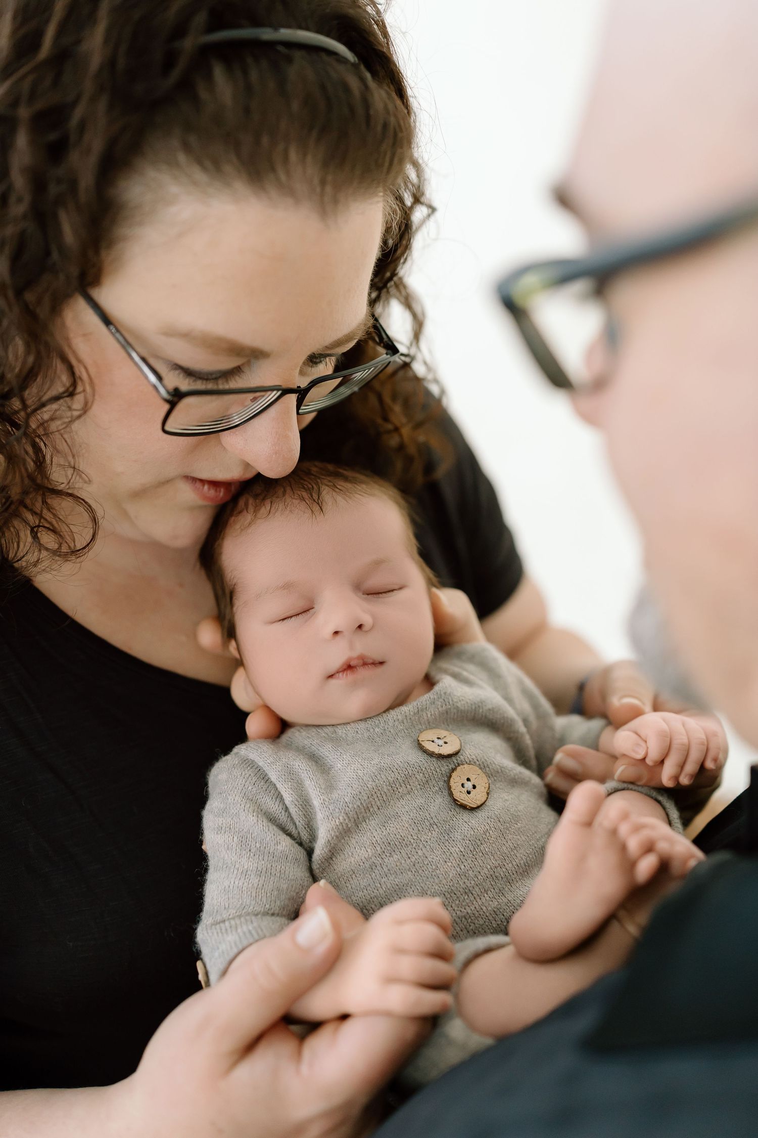 A sleeping baby in a gray onesie with wooden buttons rests peacefully in a caregiver's arms.
