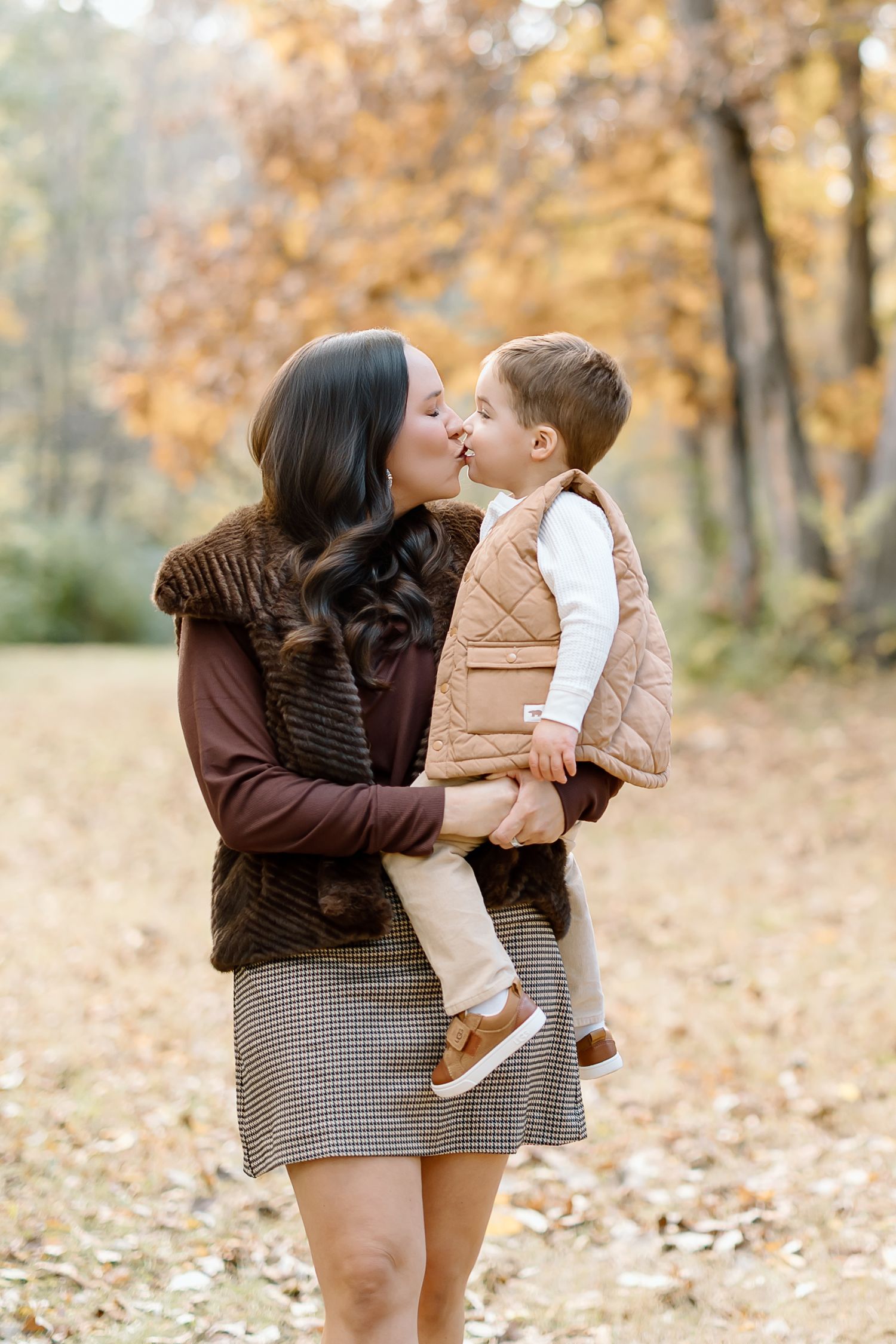 Mother and child share tender moments in an autumn forest setting with fallen leaves and golden light.