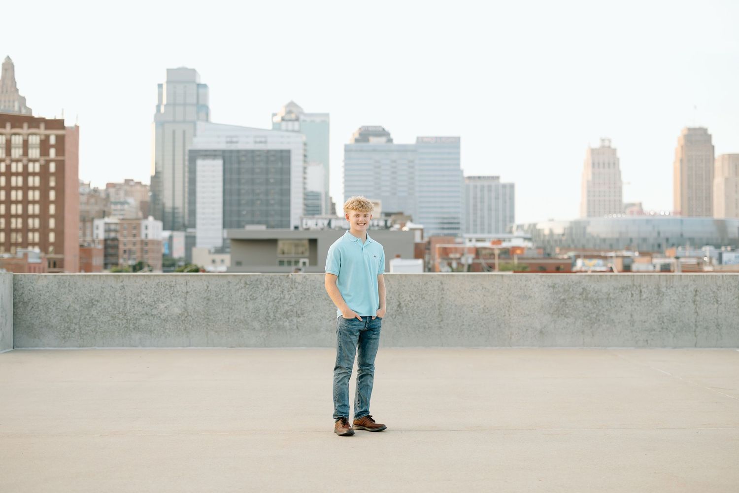 Person wearing jeans and blue shirt stands on urban rooftop with city skyline in background.