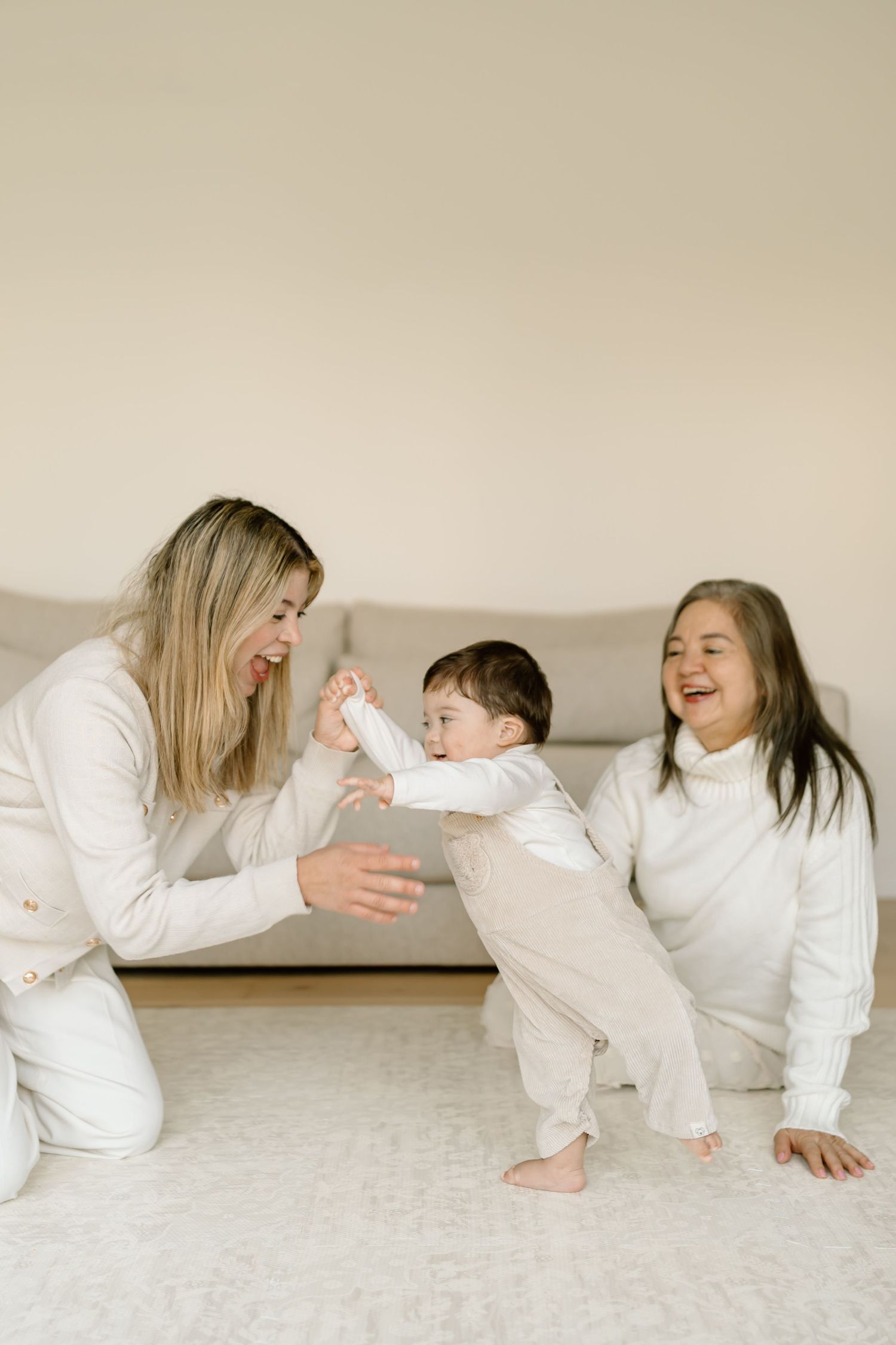 A family in white clothing shares a playful moment together on the floor, laughing and bonding.