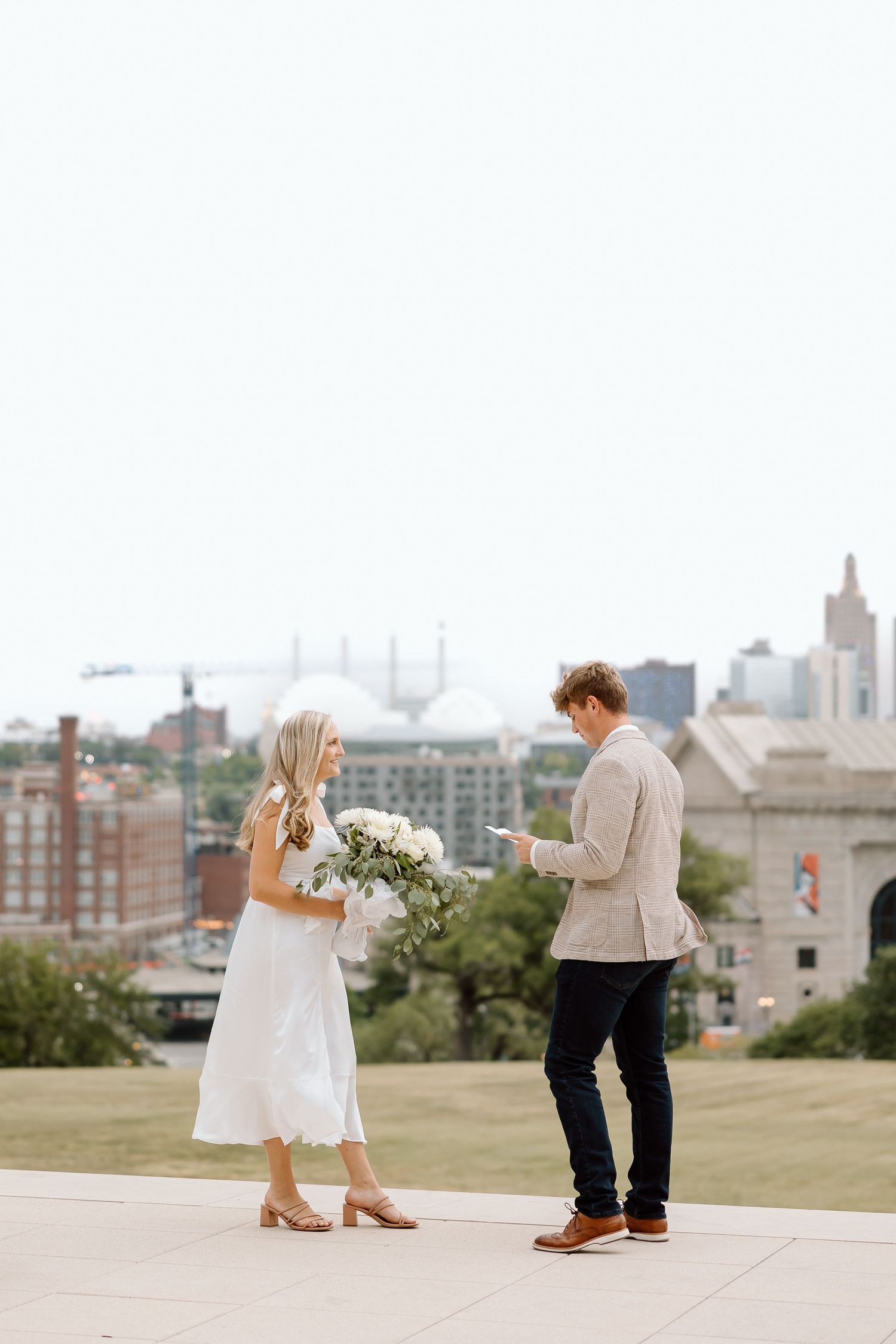 A couple dances together on a hilltop overlooking a cityscape during a romantic photo session.