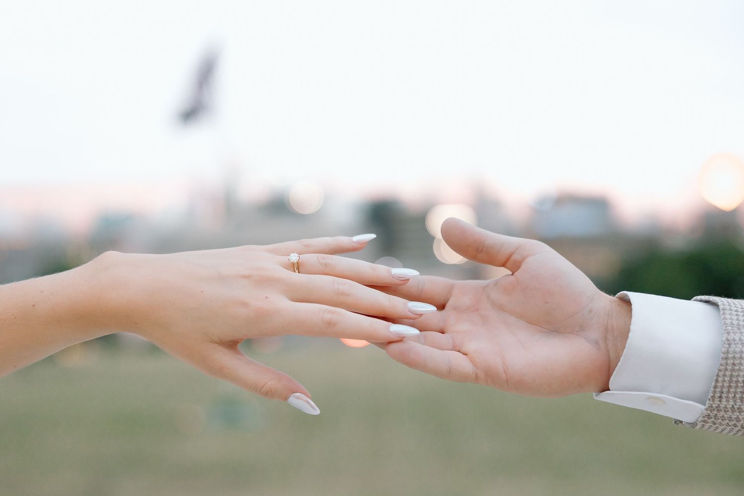 Two hands reaching towards each other against a blurred outdoor background at sunset.