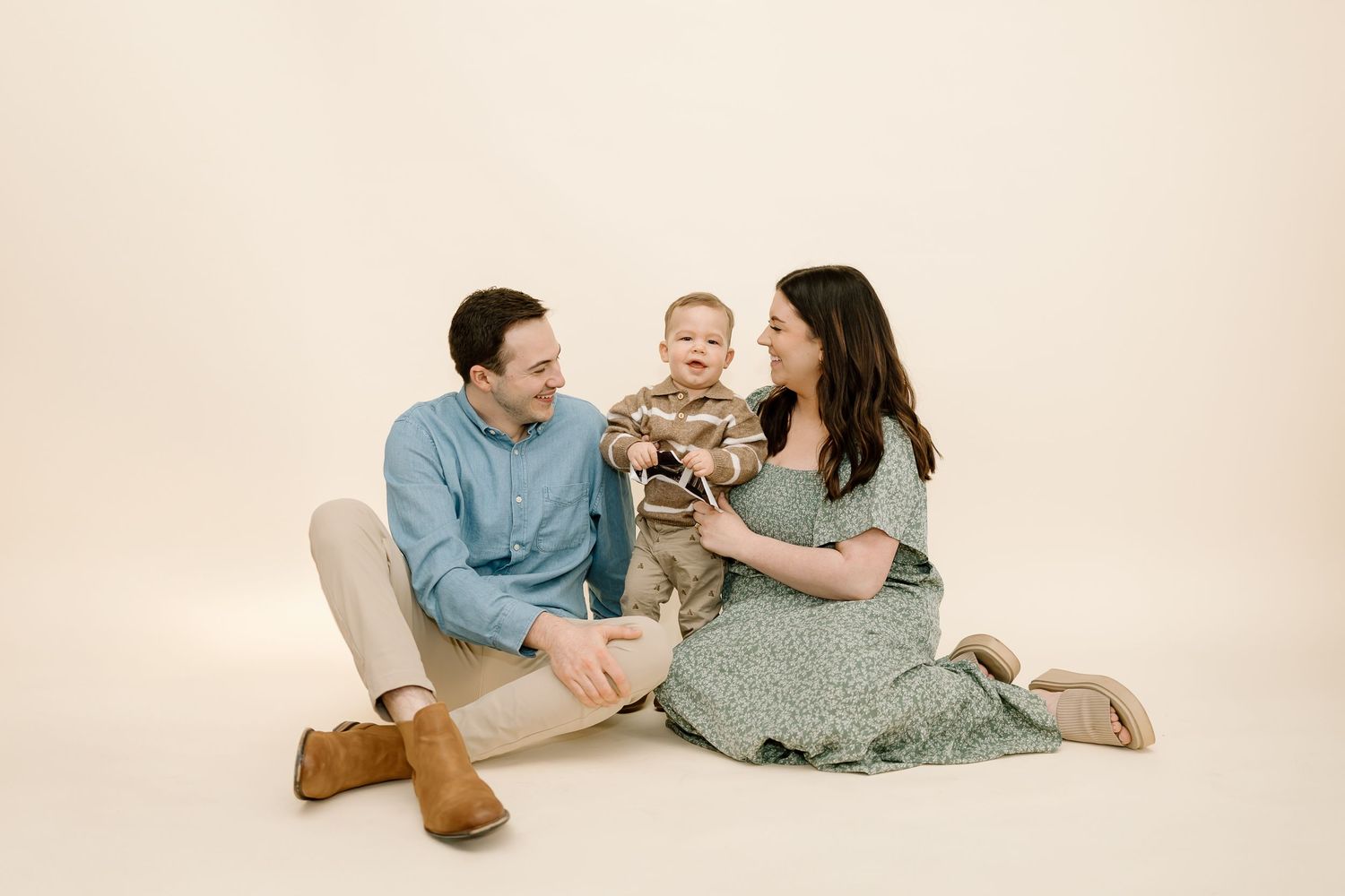 A family sits together on a beige backdrop wearing coordinated casual outfits in soft blue and sage green tones.