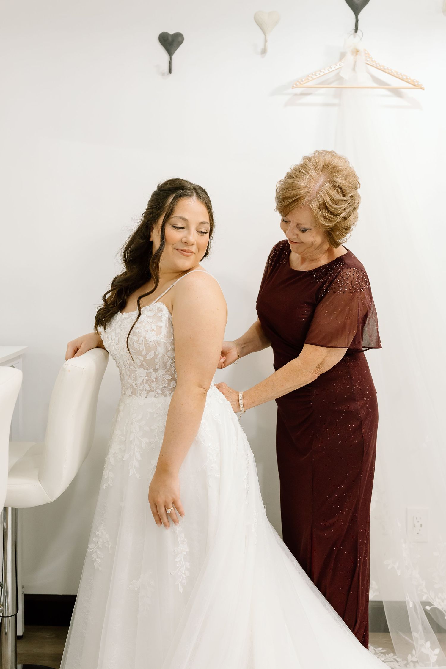 A tender moment during wedding dress fitting shows two people in a bridal boutique with heart decorations on the wall.