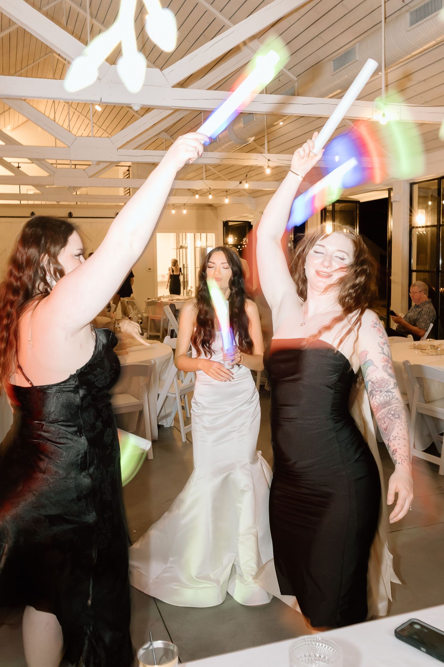 People dancing and celebrating at an indoor event venue with bright lighting and wooden beam ceiling.