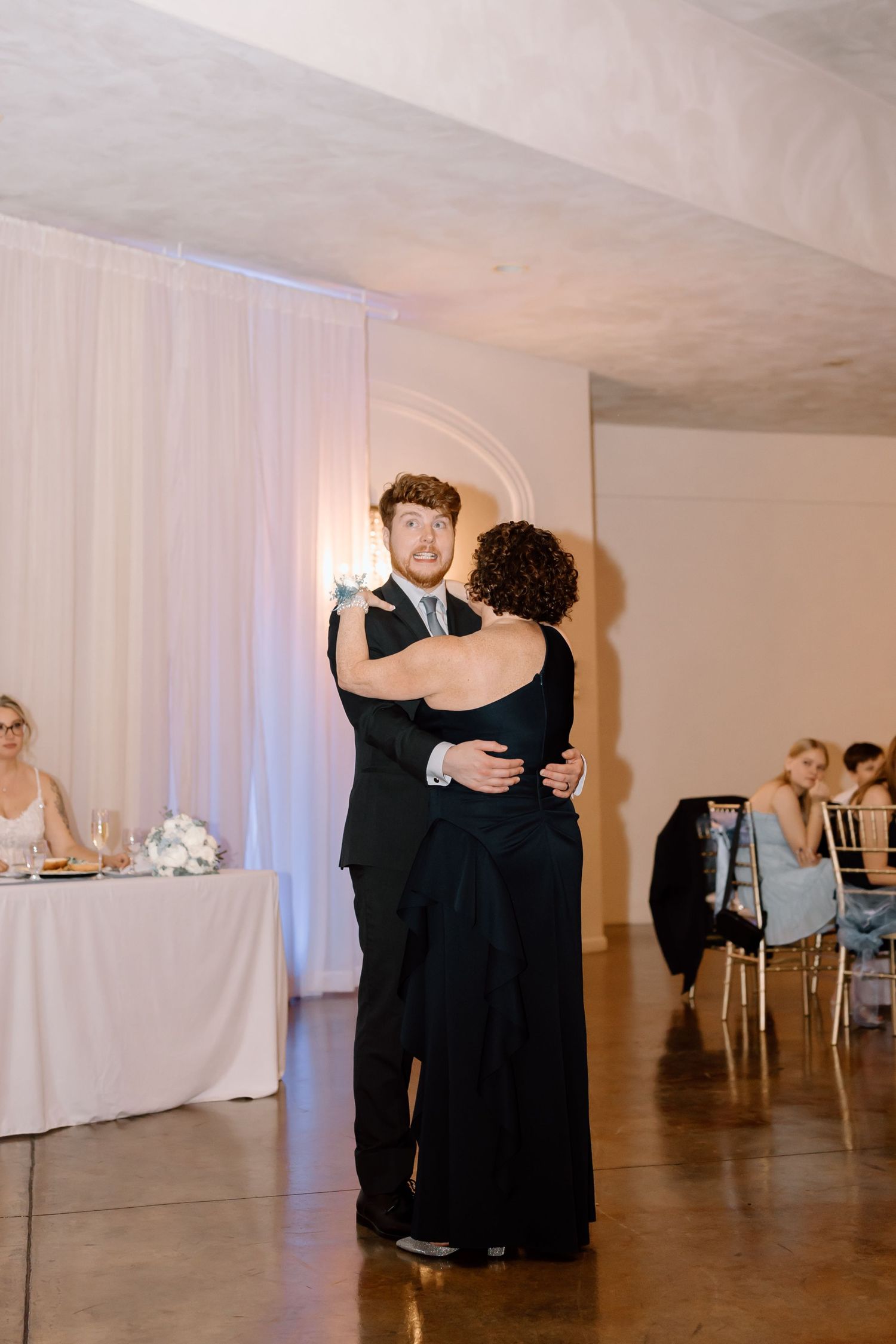 Formal event with dancers in black attire moving across a spacious ballroom with white draped walls.