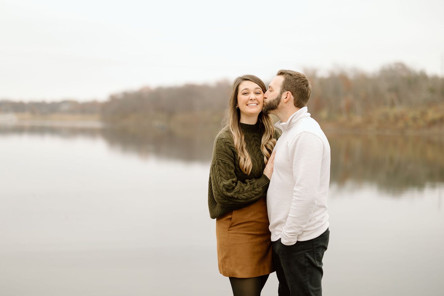 Couple shares intimate moment on wooden dock overlooking peaceful lake in autumn.