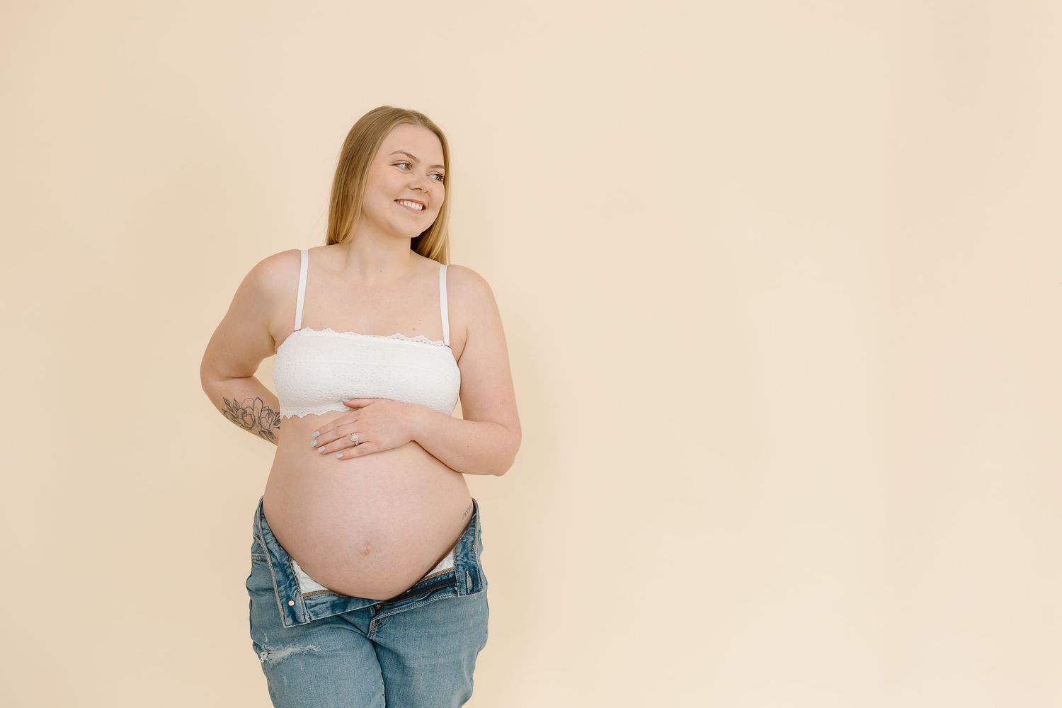 Natural maternity portrait shows expecting mother's joy against beige background.