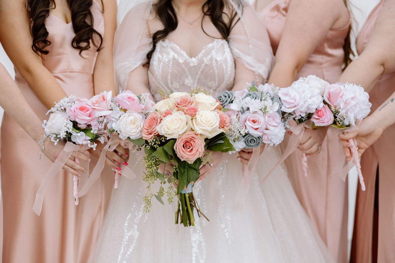 Close-up of pink and white floral bouquets held by bridesmaids in blush dresses.