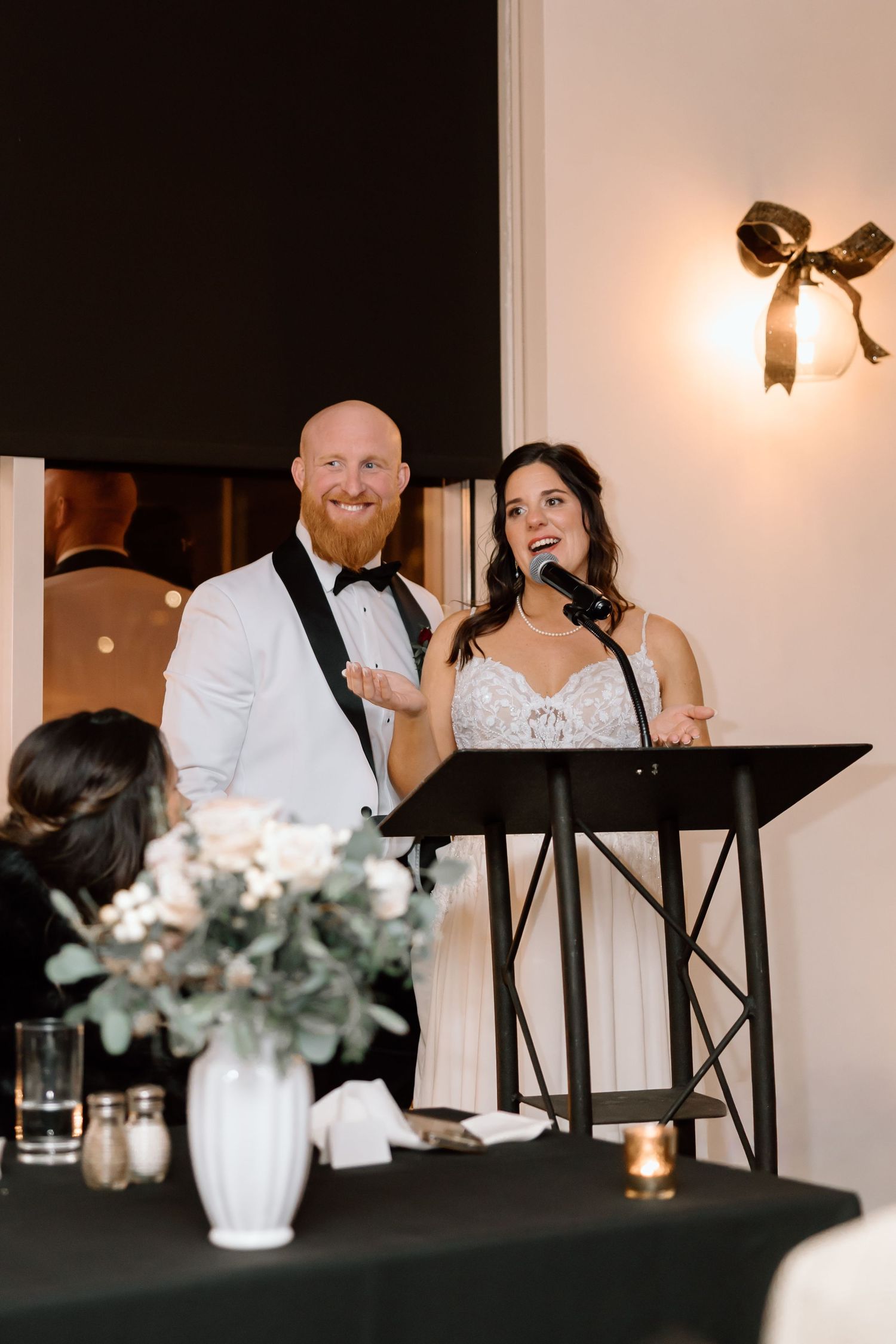 Wedding reception guests share candid moments at a formal dinner table with white floral centerpieces and elegant decor.