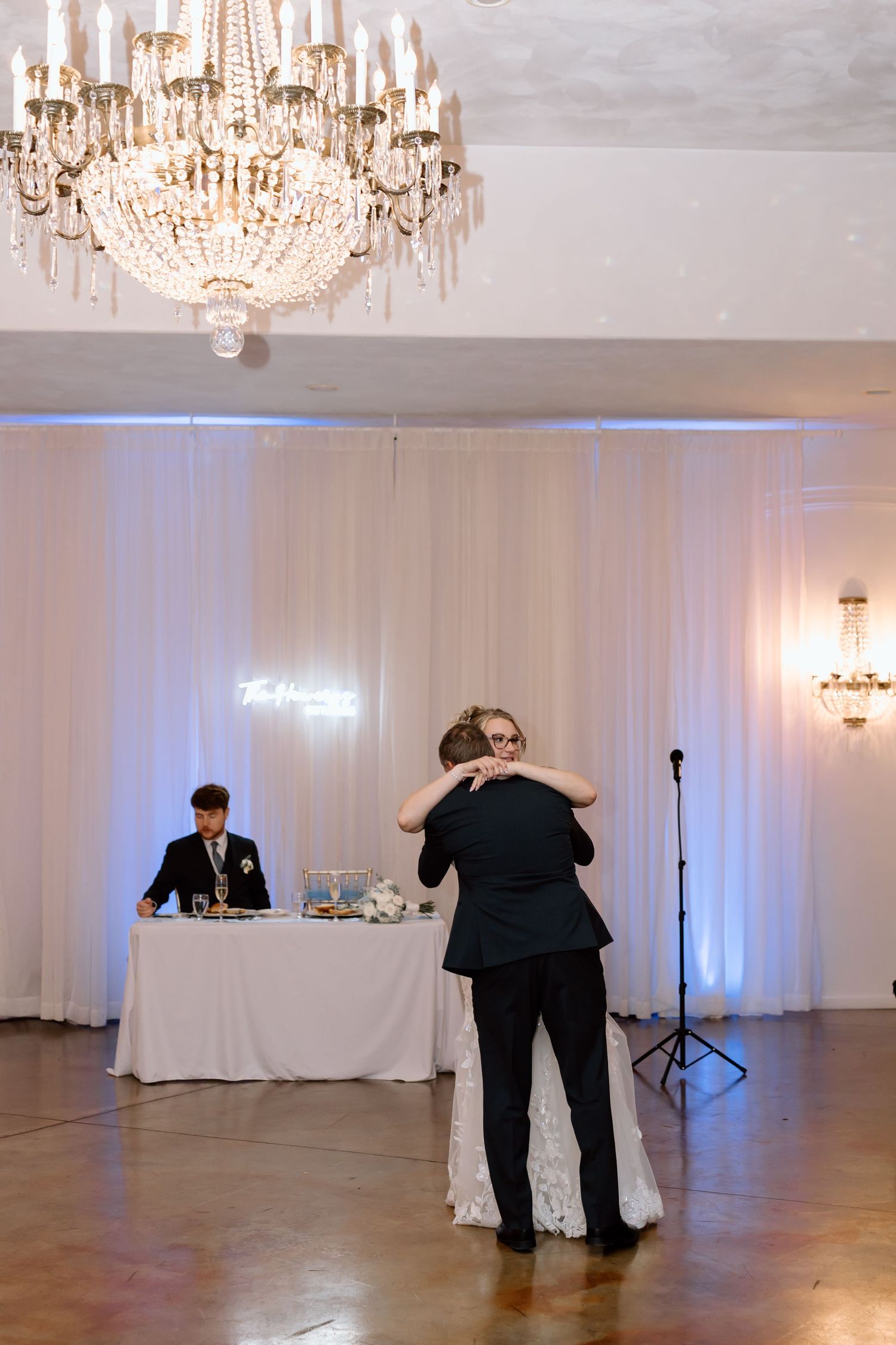 Couples dancing in an elegant ballroom with crystal chandeliers and white drapes creating a romantic atmosphere.