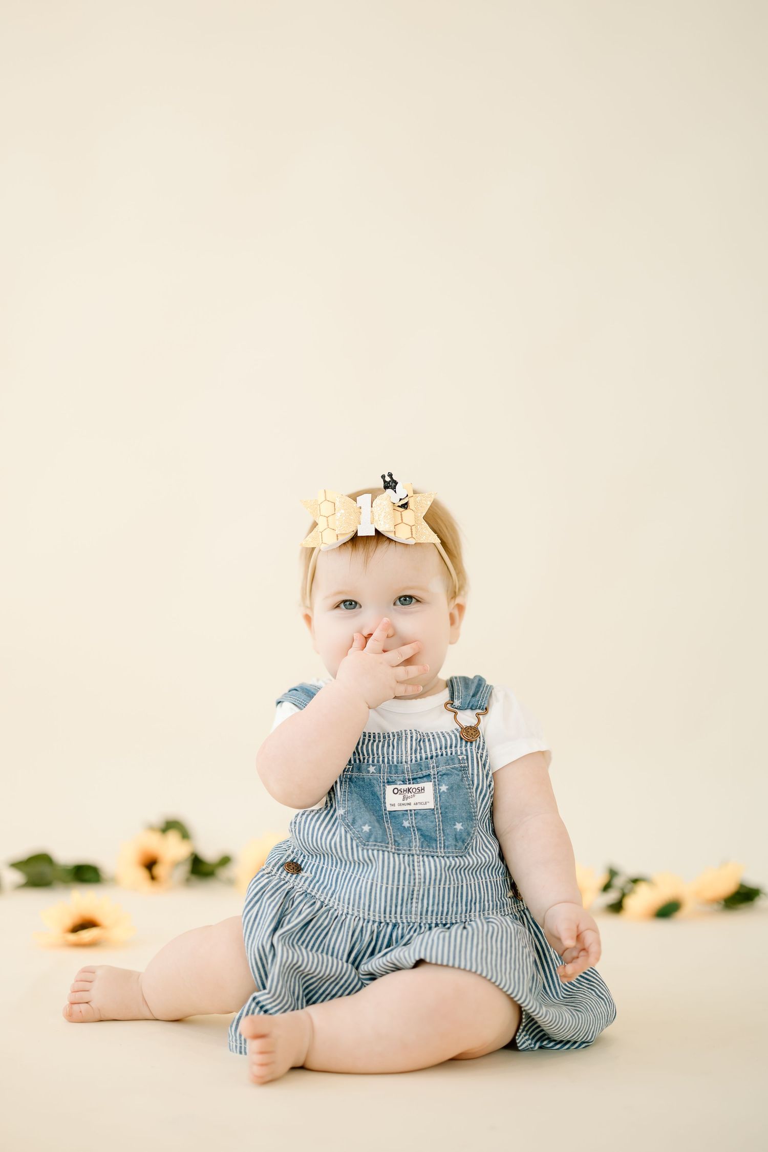 A baby wearing blue and white striped overalls sits and plays on a light colored background in a photo series.
