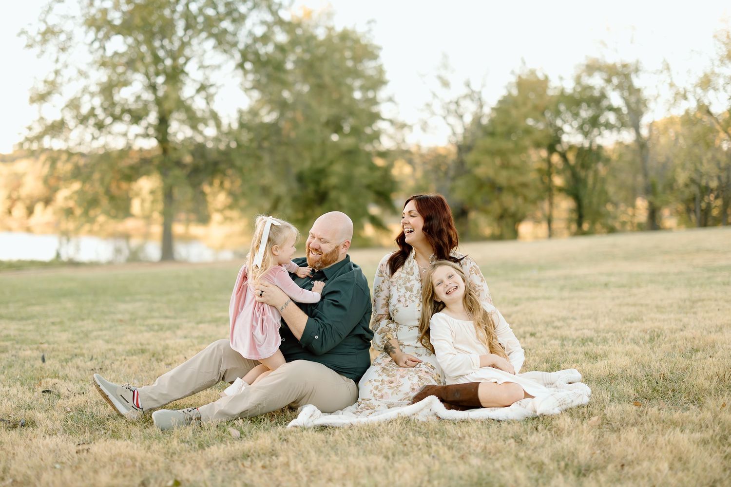 Family lounges together on a blanket in a golden grassy field during sunset for outdoor portrait session.