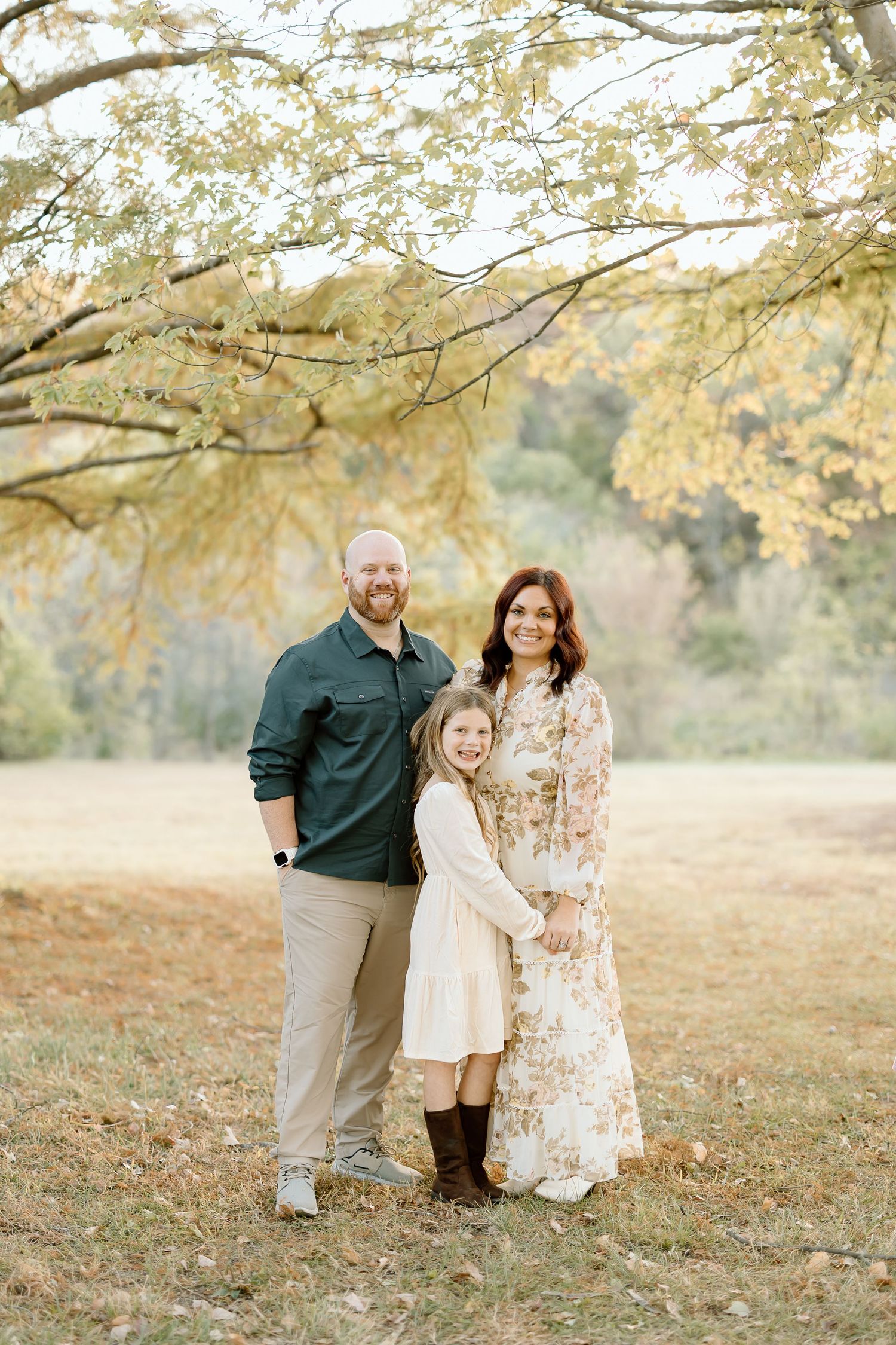 A family stands together under golden autumn trees in a field during a fall photo session.