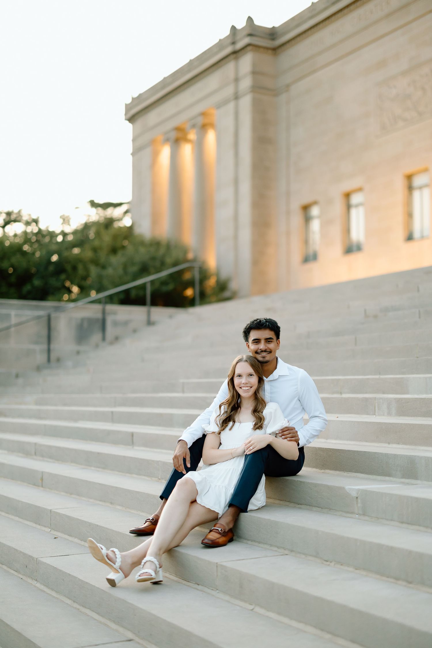 A couple lounges together on wide stone steps of a grand building during golden hour.