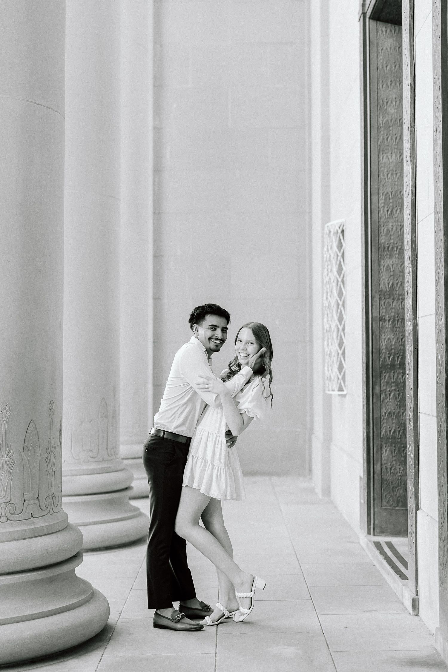 A romantic black and white photo series of a couple embracing between classical columns in an elegant setting.