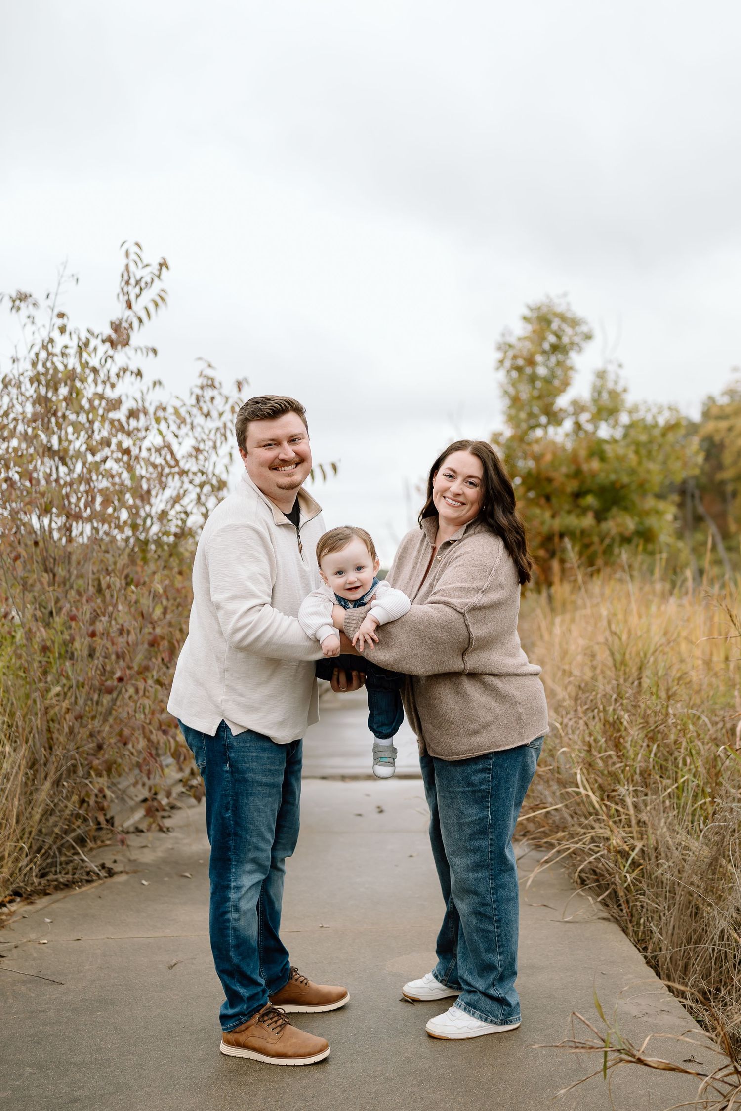 A family shares joyful moments together while posing in a field with autumn foliage during a photo session.