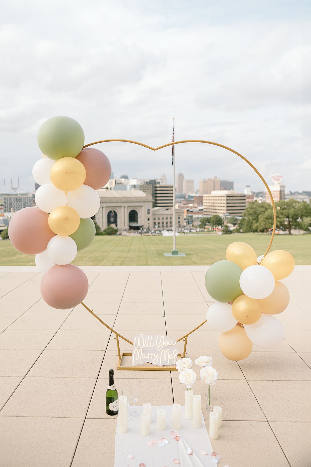 Elegant balloon arch installation with pastel colors on a rooftop overlooking a city skyline.
