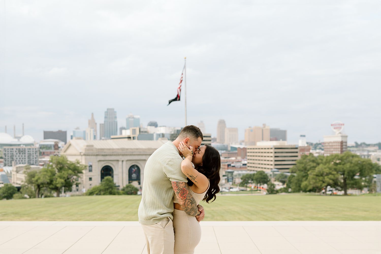 A couple shares an intimate moment overlooking the Kansas City downtown skyline on a bright day.