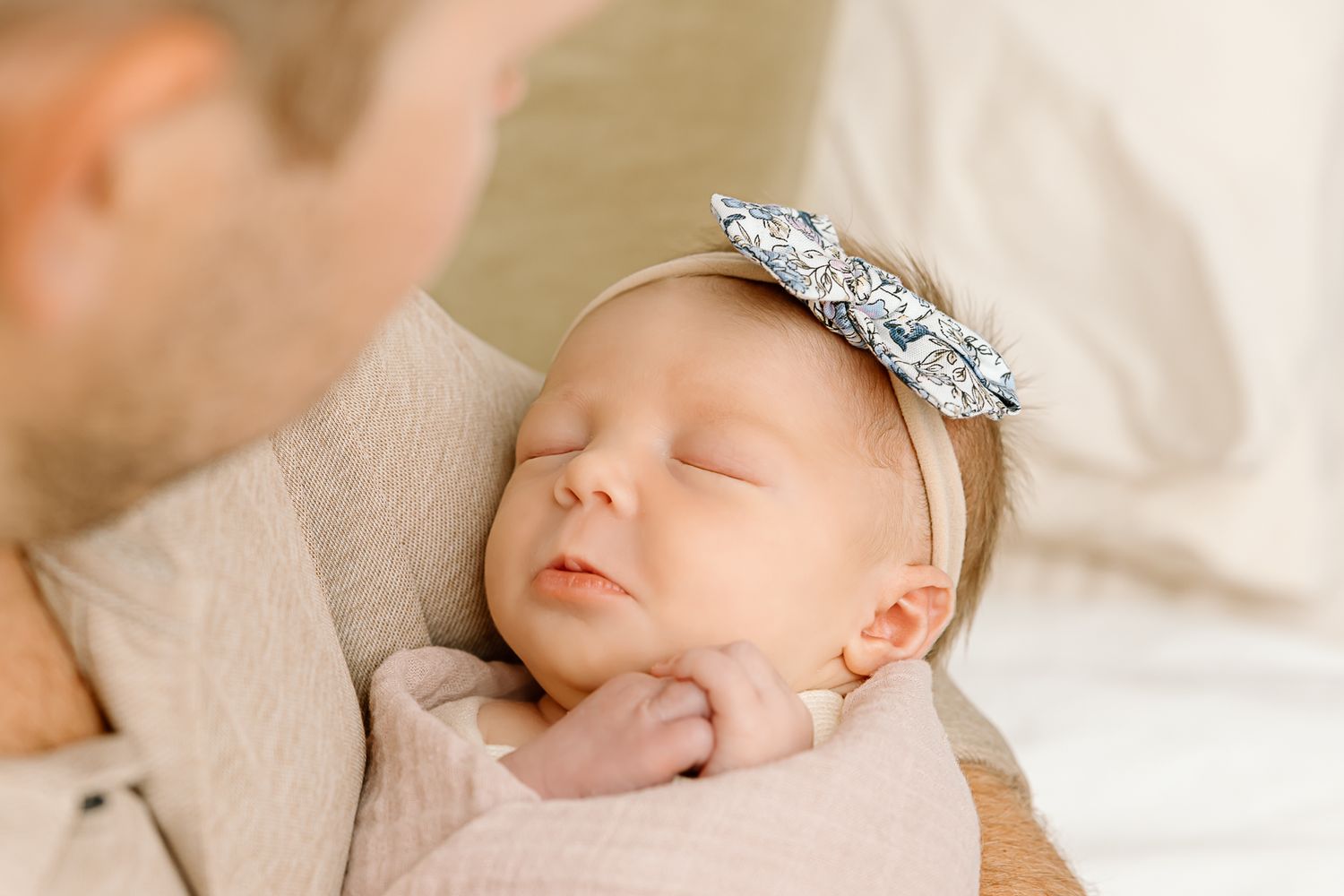 Close-up of peaceful sleeping baby wearing sparkly bow headband on adult's shoulder.