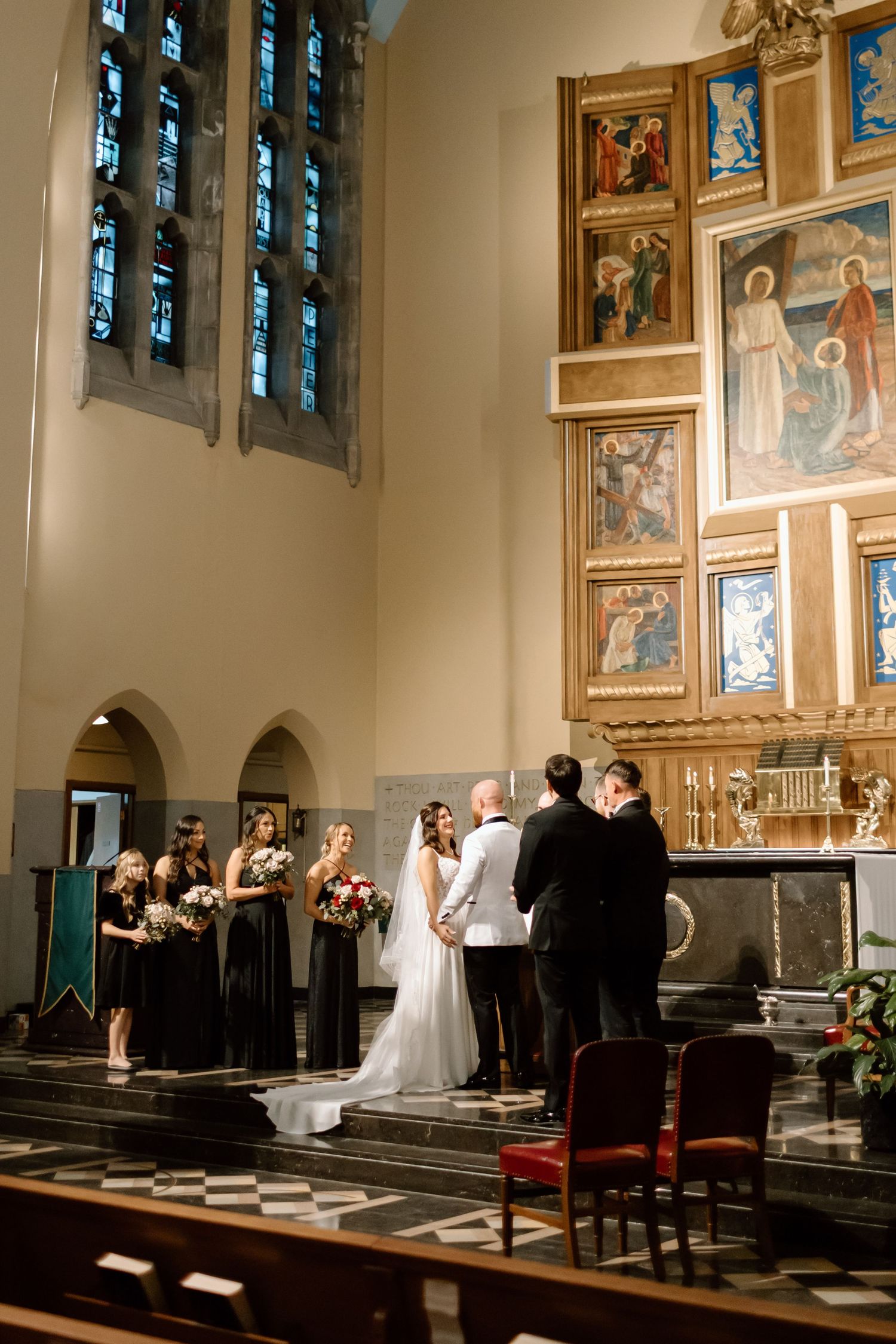 Church wedding ceremony in progress with religious artwork and stained glass windows visible in elegant chapel setting.