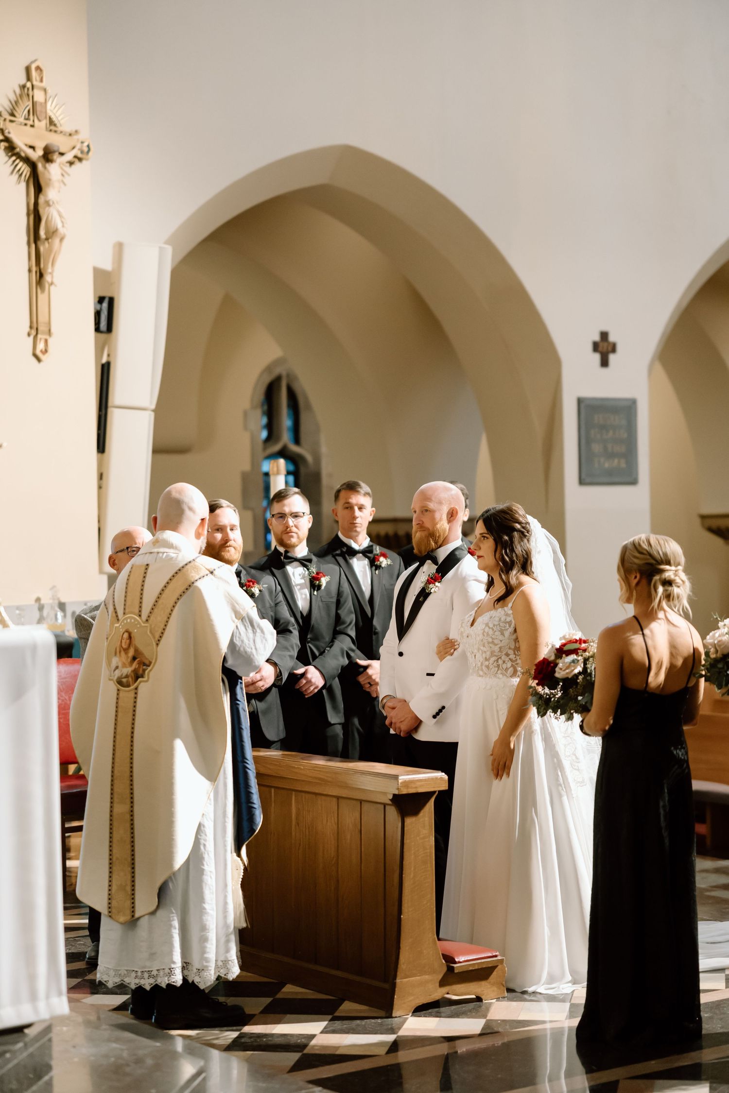 A traditional Catholic wedding ceremony takes place inside a church with arched architecture and a crucifix on the wall.