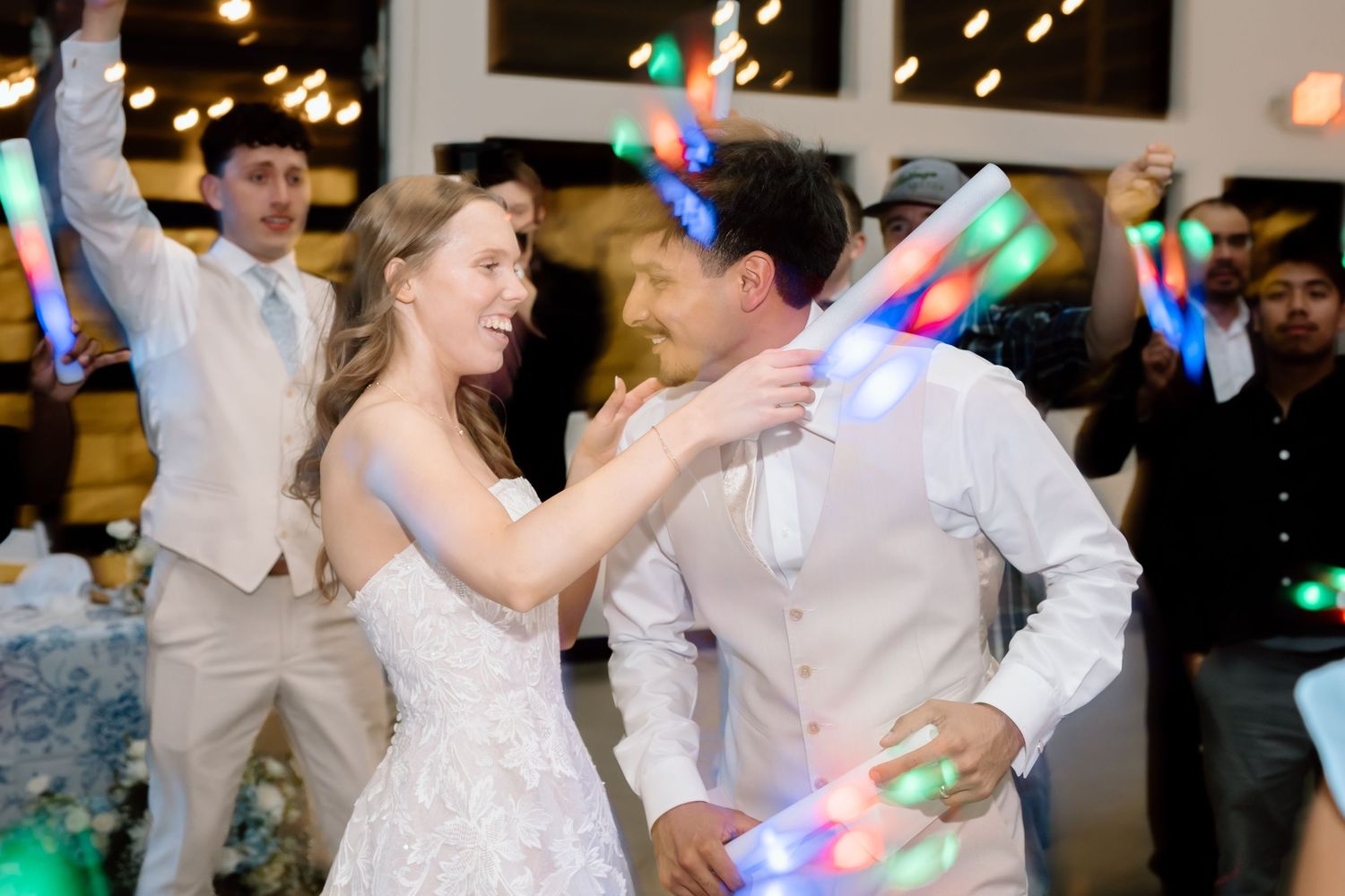 Bride and groom dancing joyfully with colorful LED glow sticks at their wedding reception celebration.