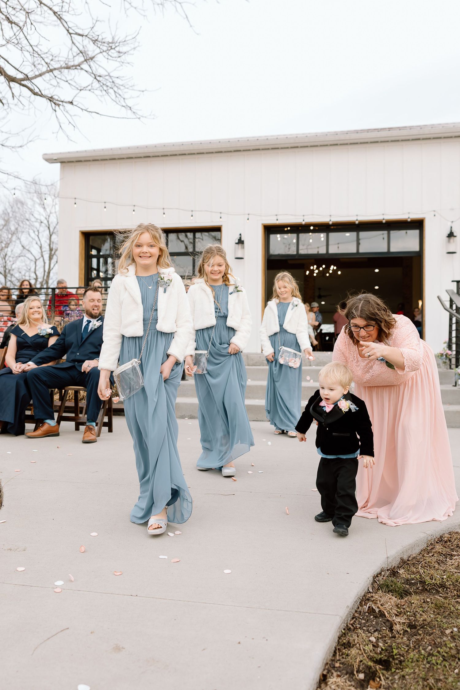 Wedding party walking down outdoor pathway wearing denim overalls with white tops and a pink gown.