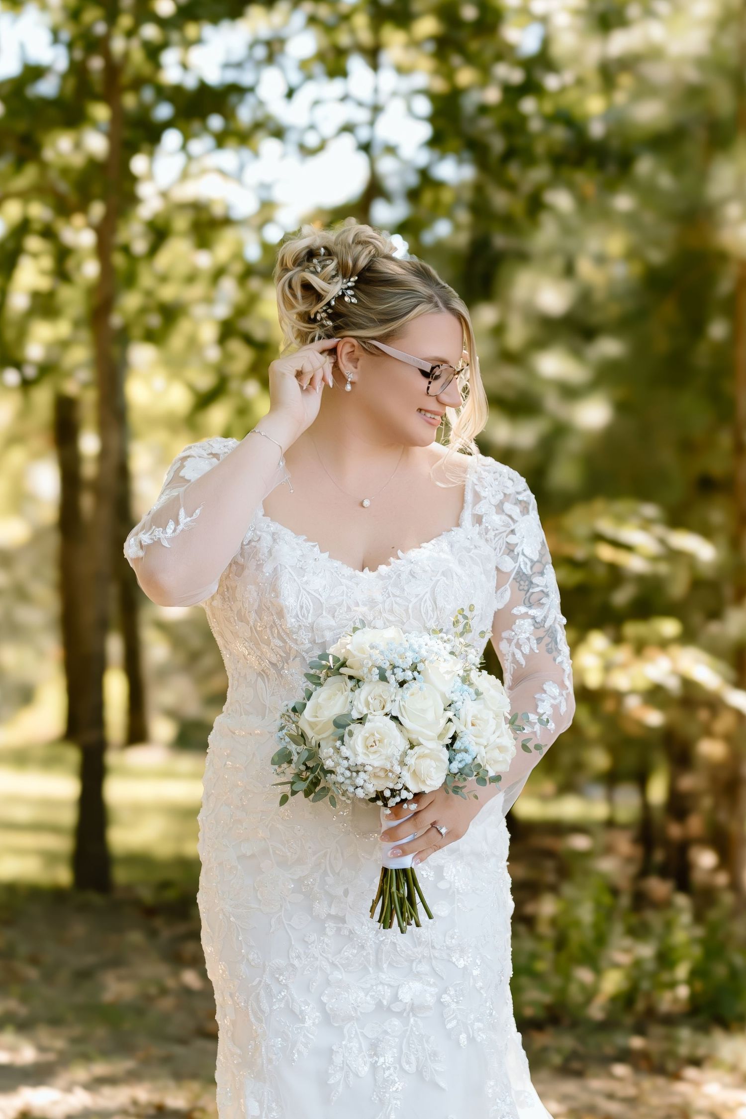 Beautiful lace wedding dress with long sleeves and white floral bouquet captured in a sunlit outdoor setting.